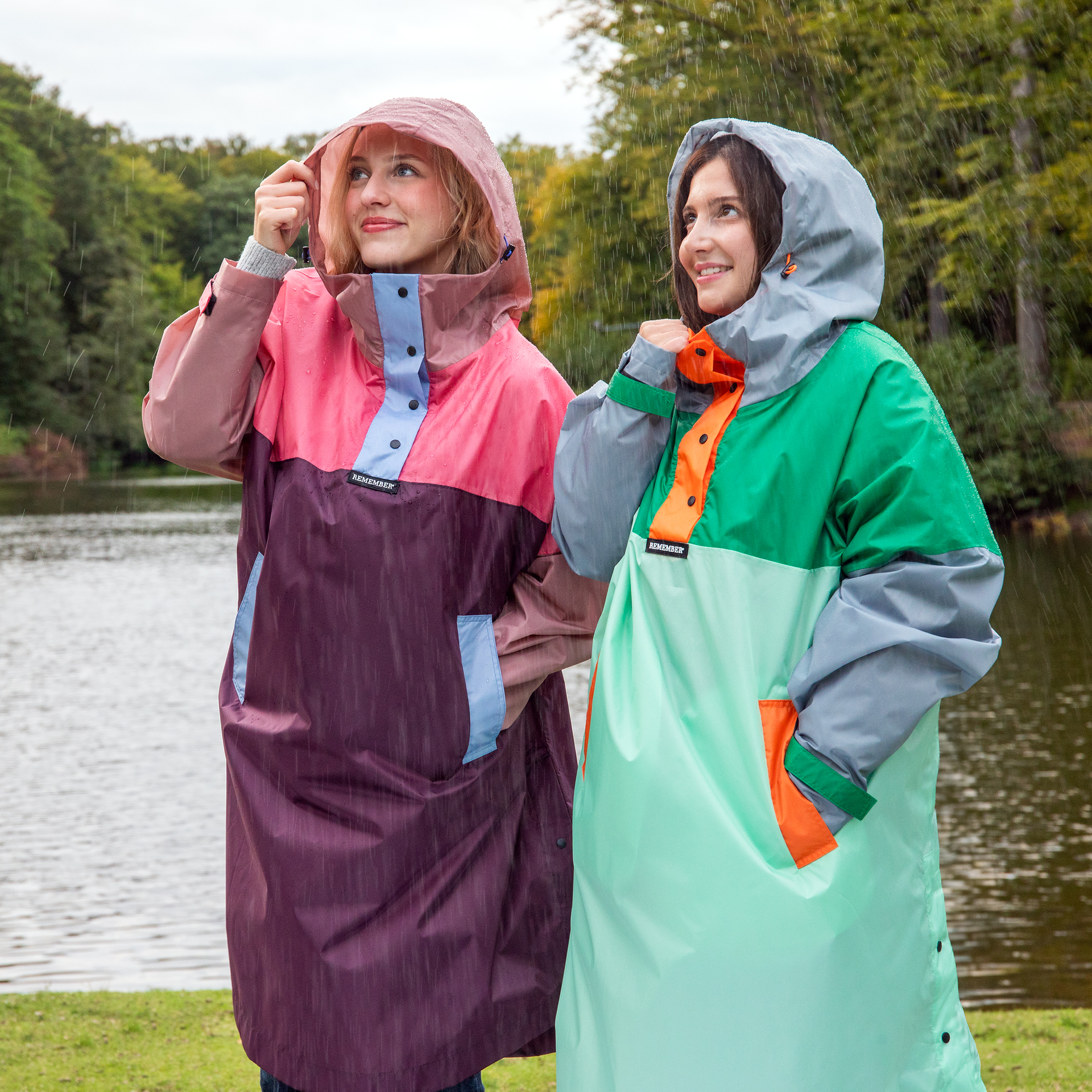 Freigestelltes, farbiges Regencape Max in Grün, Grau und Mint mit orangefarbenen Akzenten und Druckknöpfen. Kapuze und seitliche Eingrifftaschen sind erkennbar.