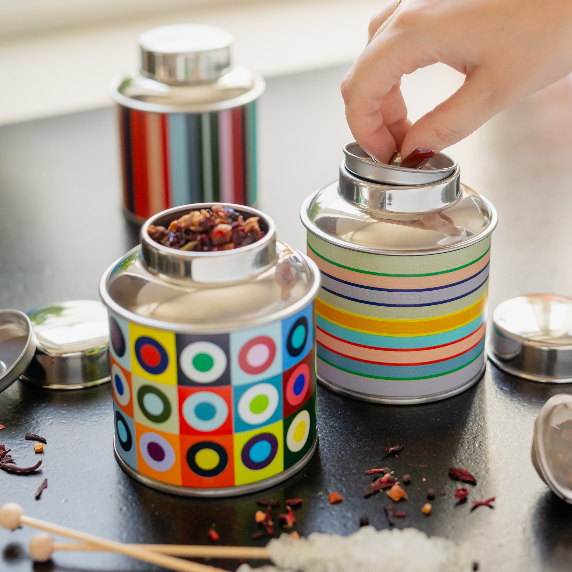Scatola da tè cilindrica con coperchio argentato lucido e corpo dai colori vivaci. Con strisce orizzontali dai toni pastello nei colori beige, verde, rosa, viola, blu, giallo, arancione e rosso, nel design " REMEMBER". In acciaio inossidabile.