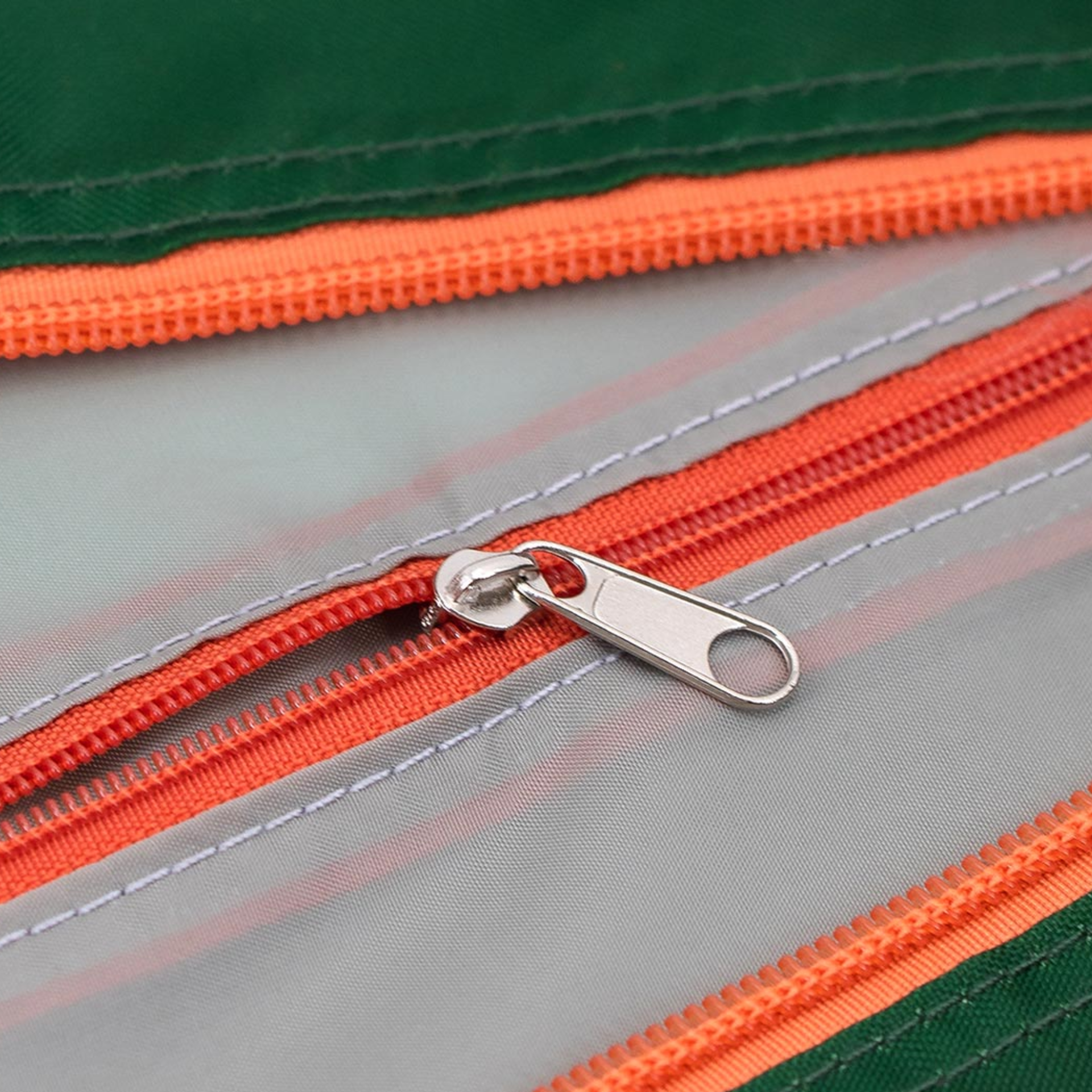 Detailaufnahme einer 'Max' Reisetasche: Reißverschluss ist geöffnet, silberner Zipper liegt auf hellgrauem Stoff. Nähte und orangefarbene Reißverschlüsse sind zu sehen.