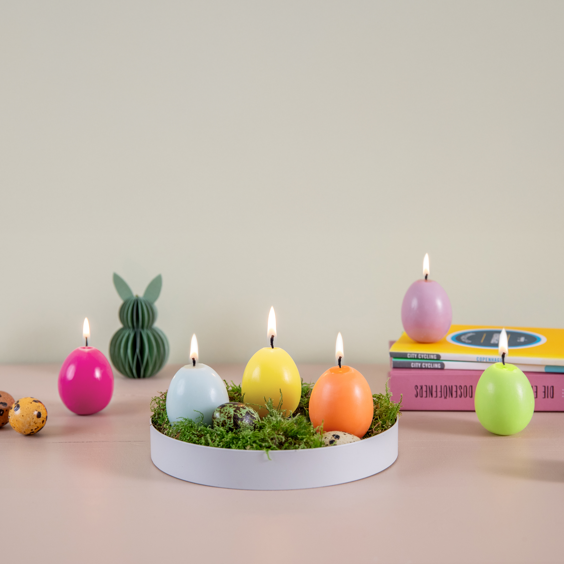 Ein 6er-Set Eierkerzen in einem offenen Eierkarton. Die Kerzen sind in Gelb, Orange, Rosa, Grün, Hellgrün und Lila gefärbt.