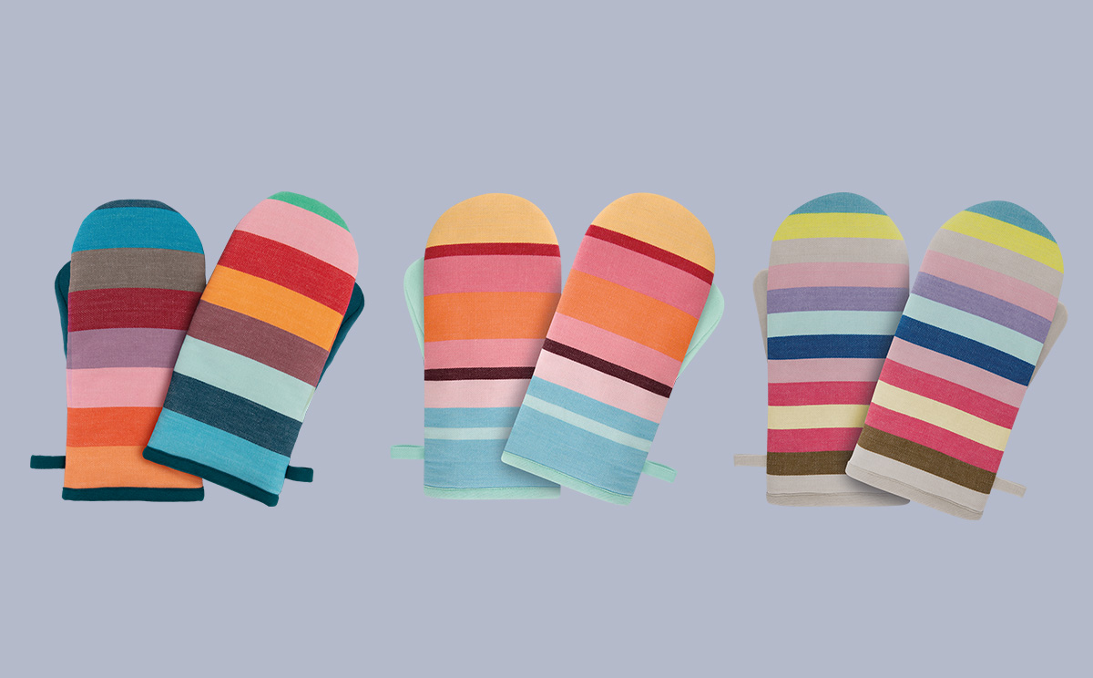 Drei Paare bunter Ofenhandschuhe mit horizontalen Streifen liegen schräg auf hellgrauem Hintergrund. Die Handschuhe zeigen Farbkombinationen wie Türkis, Braun, Rosa, Orange, Rot, Gelb und Lila mit fröhlichen Mustern.