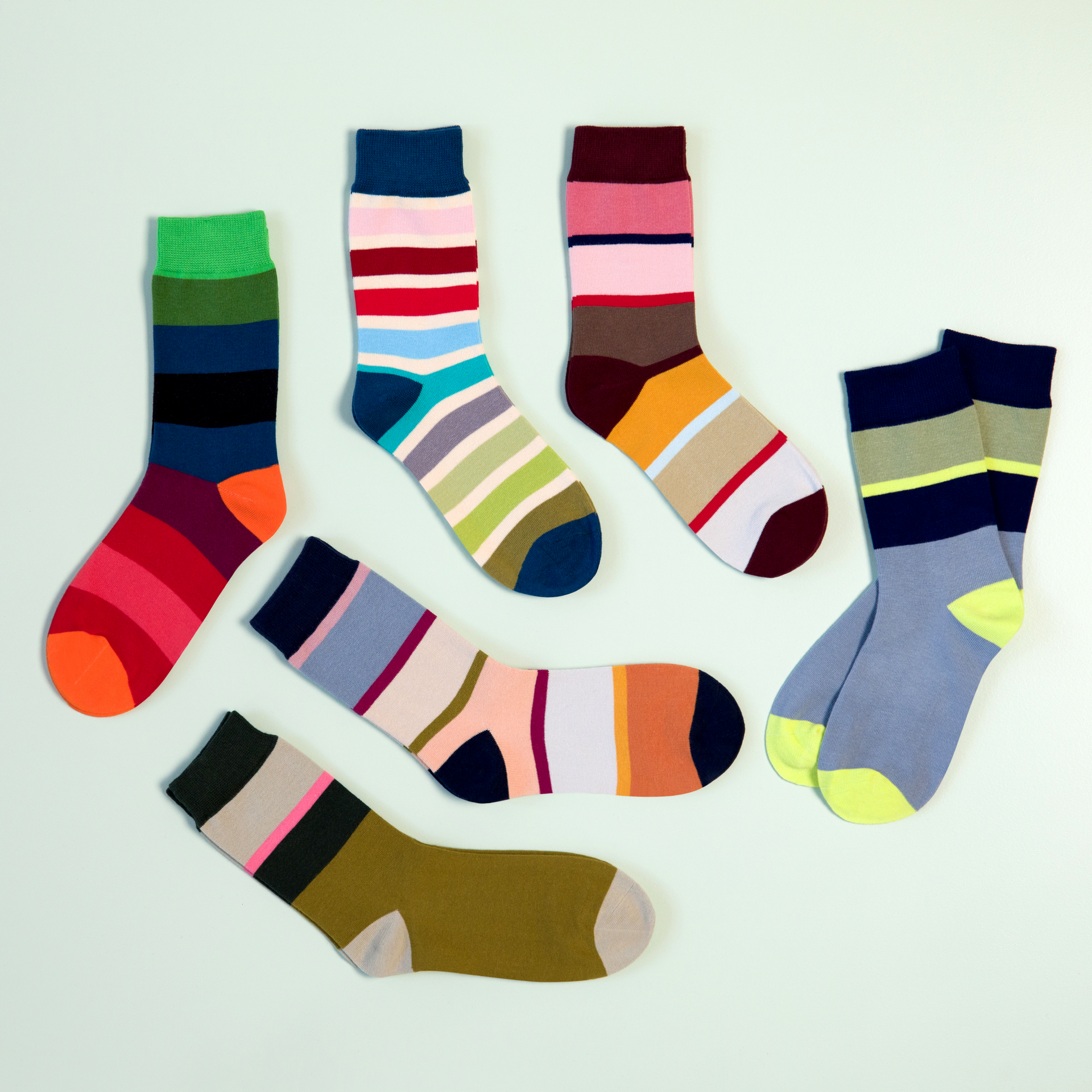 Verschiedene farbenfrohe Socken, Modell 61, Größe 36-41, mit Streifen- und Blockfarbenmuster liegen auf hellblauem Grund.