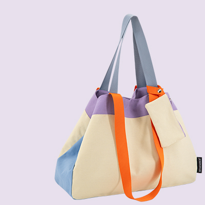 Eine farbenfrohe Tragetasche mit blauem, beigem und lilafarbenem Blockmuster. Sie verfügt über orangefarbene Akzentbänder und graue Tragegriffe. Eine kleine beige Tasche ist befestigt.