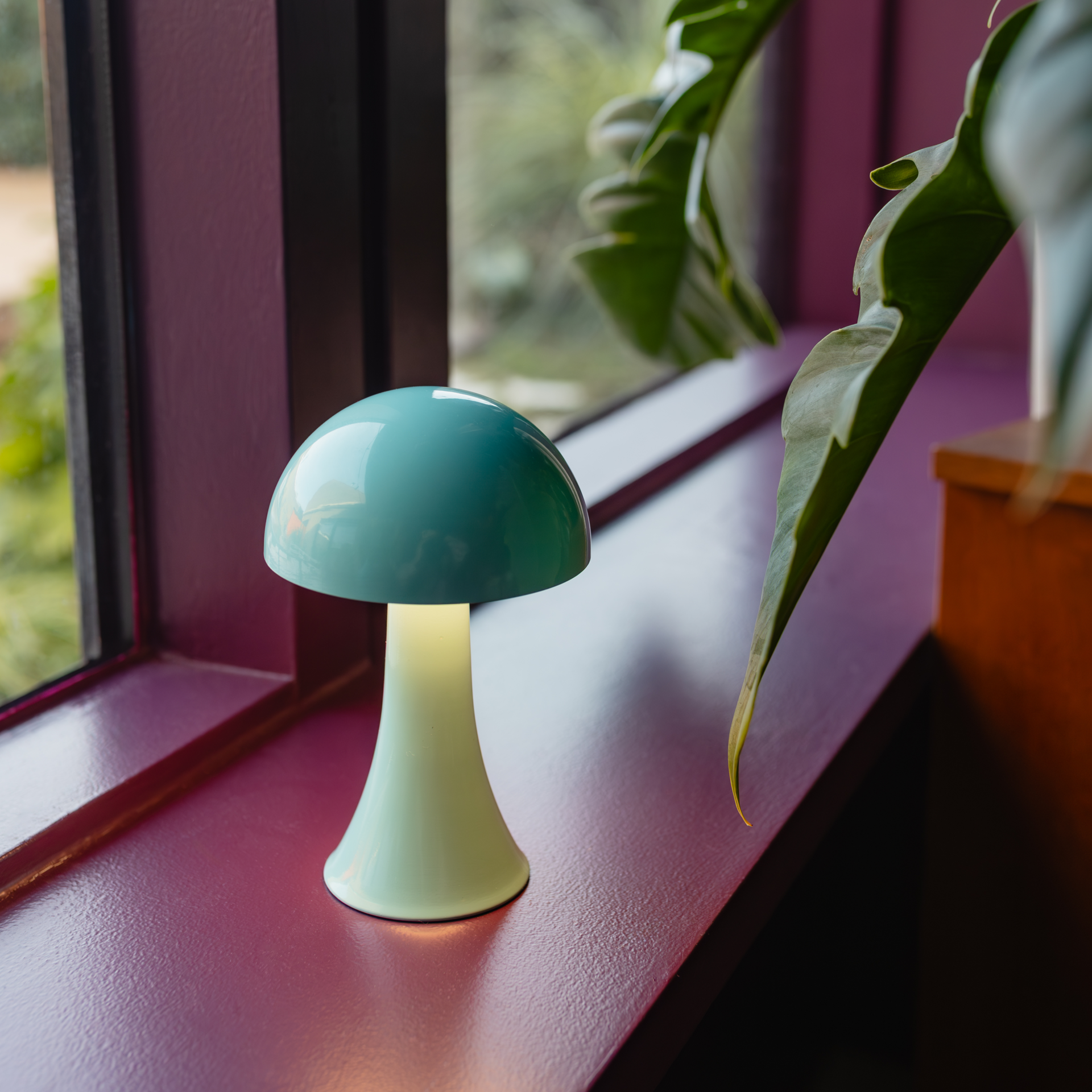 Türkis-blaue Mini-Leuchte Filou mit glänzendem, kuppelförmigem Schirm und schlankem Fuß auf weißem Grund.