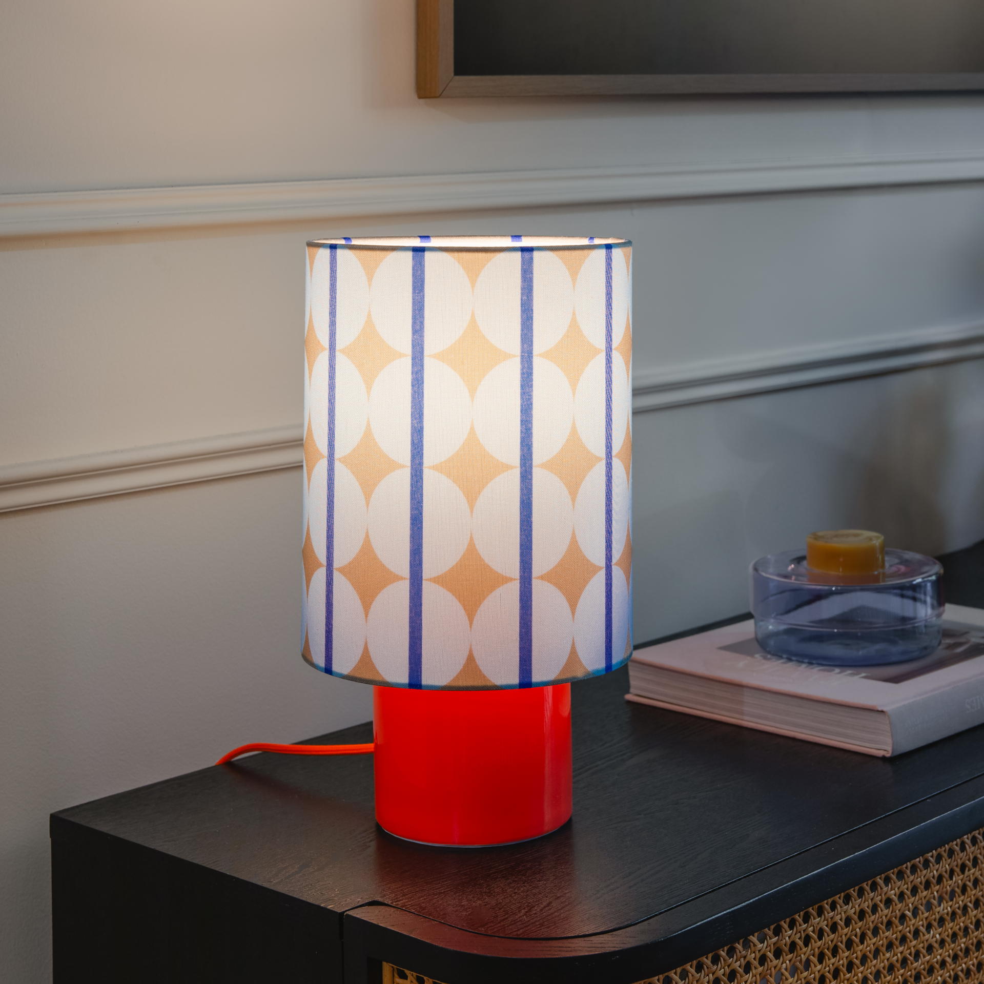 Zylindrische Tischlampe mit leuchtend orangefarbenem Keramikfuß. Textil-Lampenschirm mit modernem Muster aus überlappenden hellblauen Kreisen auf beigem Grund, mit vertikalen dunkelblauen Streifen. 36 cm hoch.