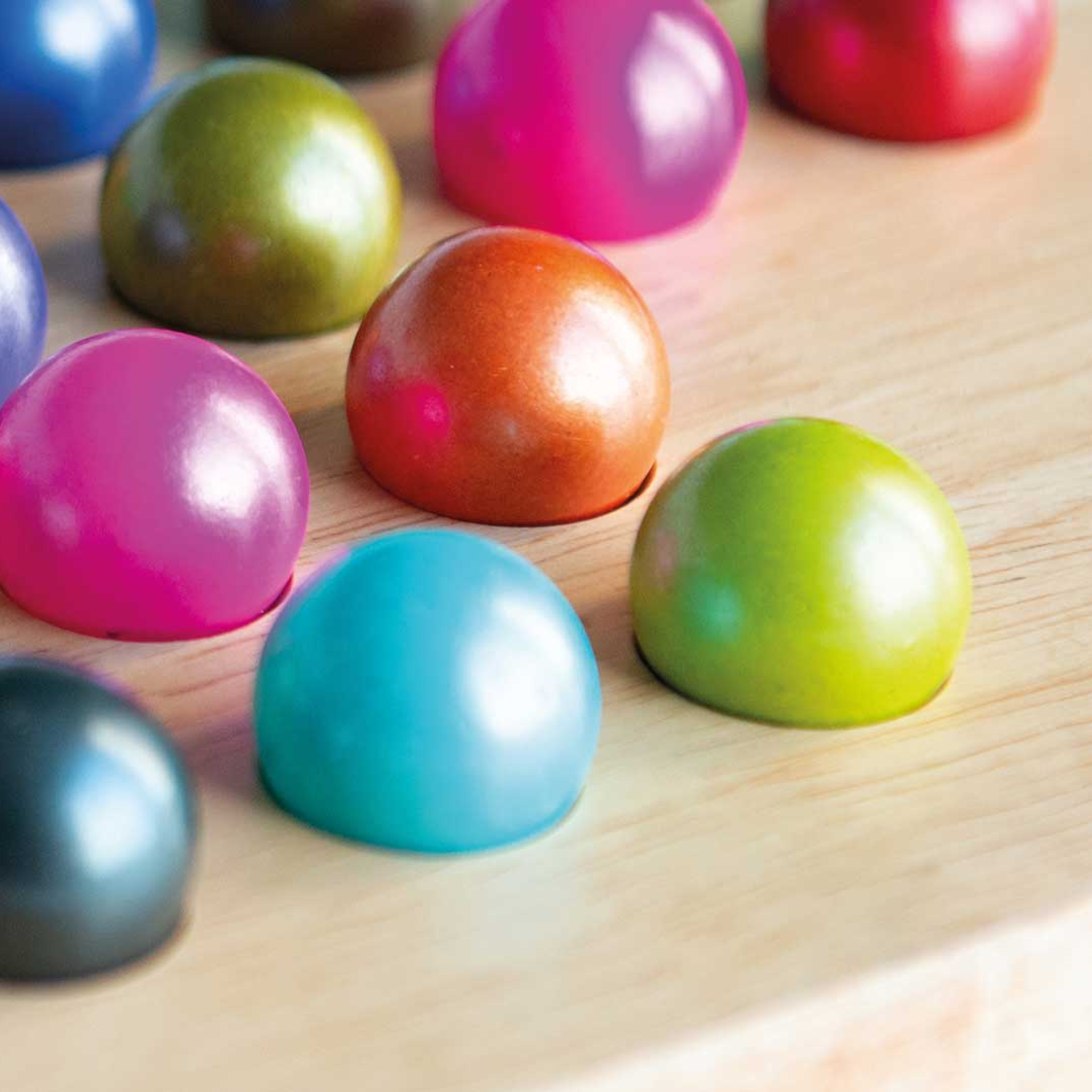Gros plan de billes de verre colorées sur un plateau en bois clair, faisant partie du jeu Solitaire. Boules de couleur bleue, verte, rose, rouge et marron.