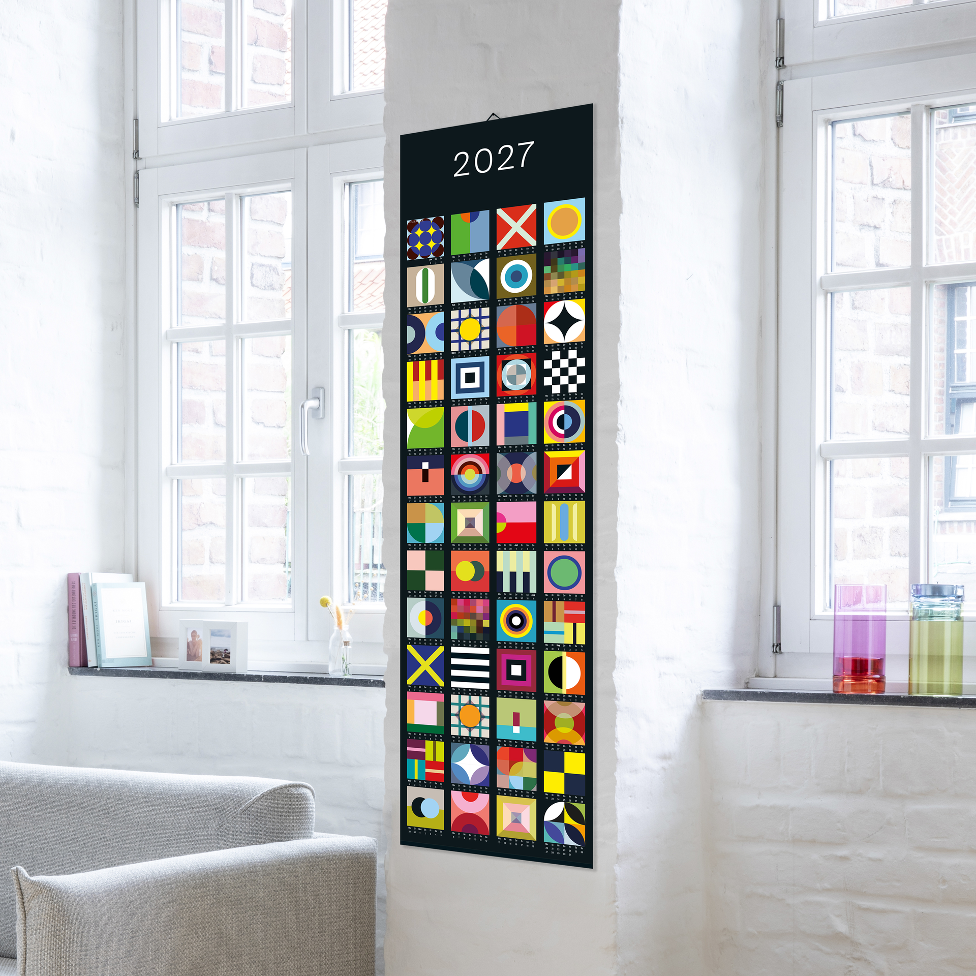 Calendrier vertical en bannière 2027 avec 52 carrés colorés et abstraits sur fond sombre. Chaque case représente une semaine et affiche des formes géométriques et motifs vivants uniques. L'année 2027 est en haut.