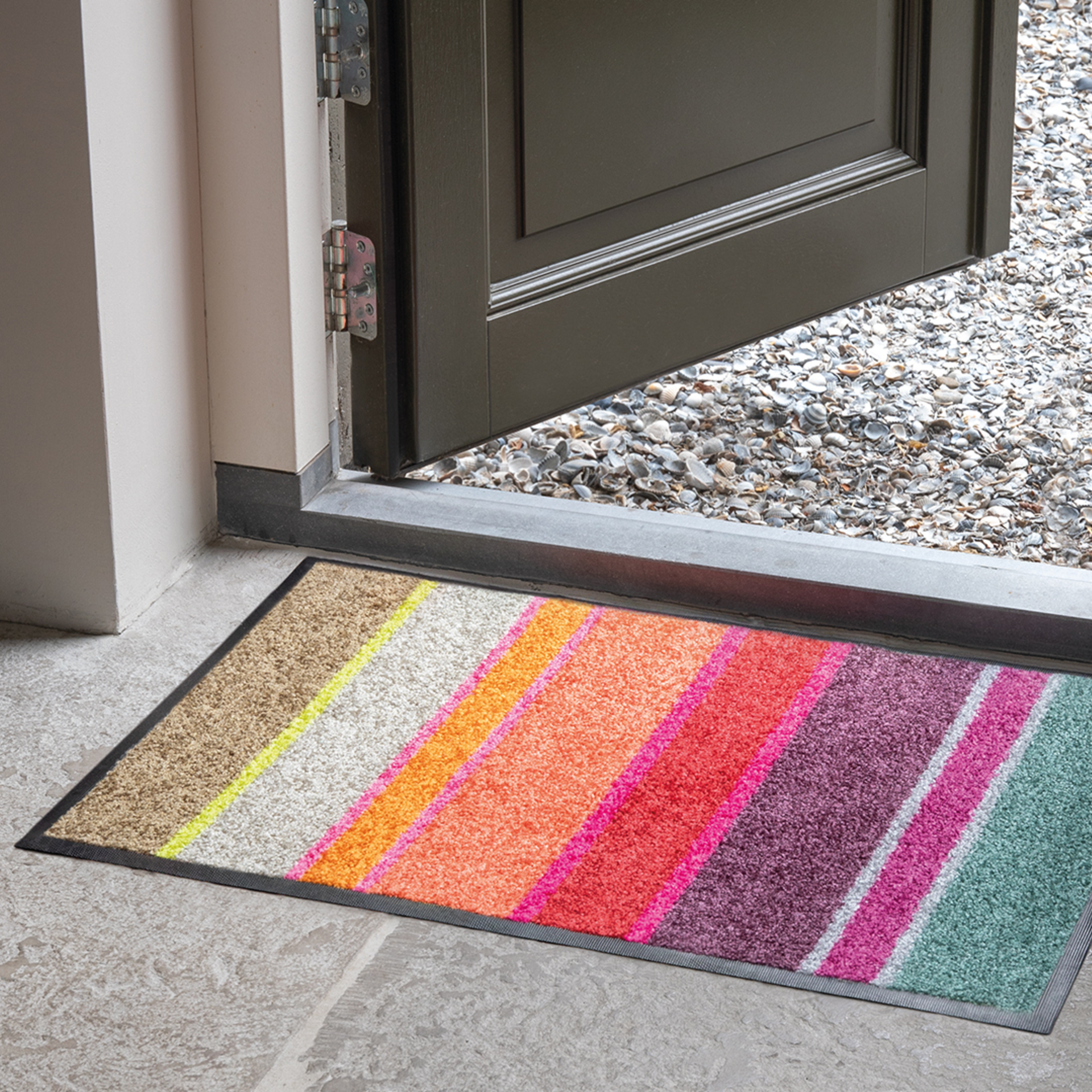 Offene Tür mit farbenfroher Fußmatte "Largo" davor. Die Matte hat diagonale Streifen in Braun, Gelb, Weiß, Orange, Pink, Rot, Lila und Türkis.