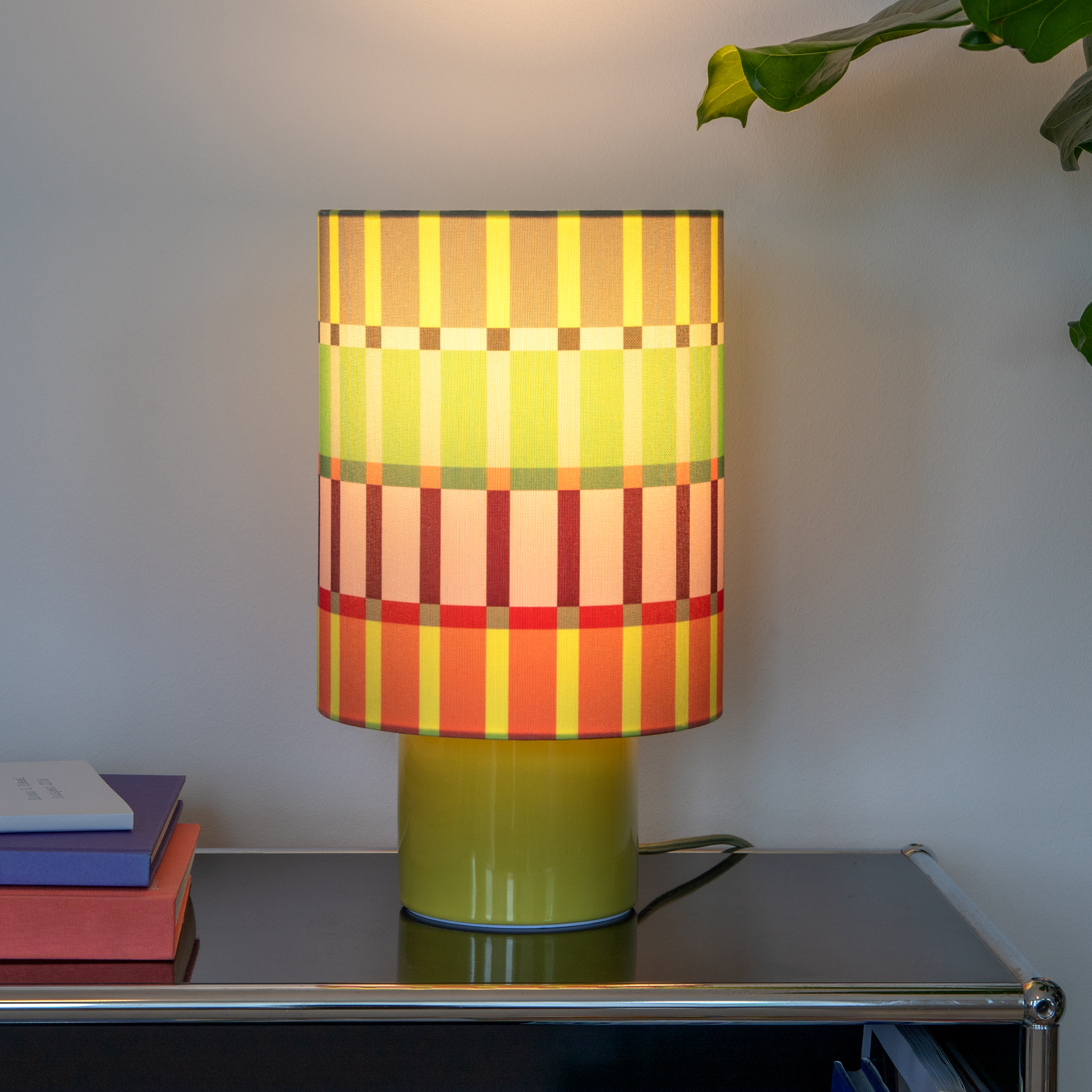 Moderne Tischleuchte mit zylindrischem Schirm und lebhaftem, geometrischem Streifenmuster in Grün, Rosa, Orange, Gelb und Grau. Zylindrischer Keramikfuß in sanftem Olivgrün, dazu passendes Textilkabel.