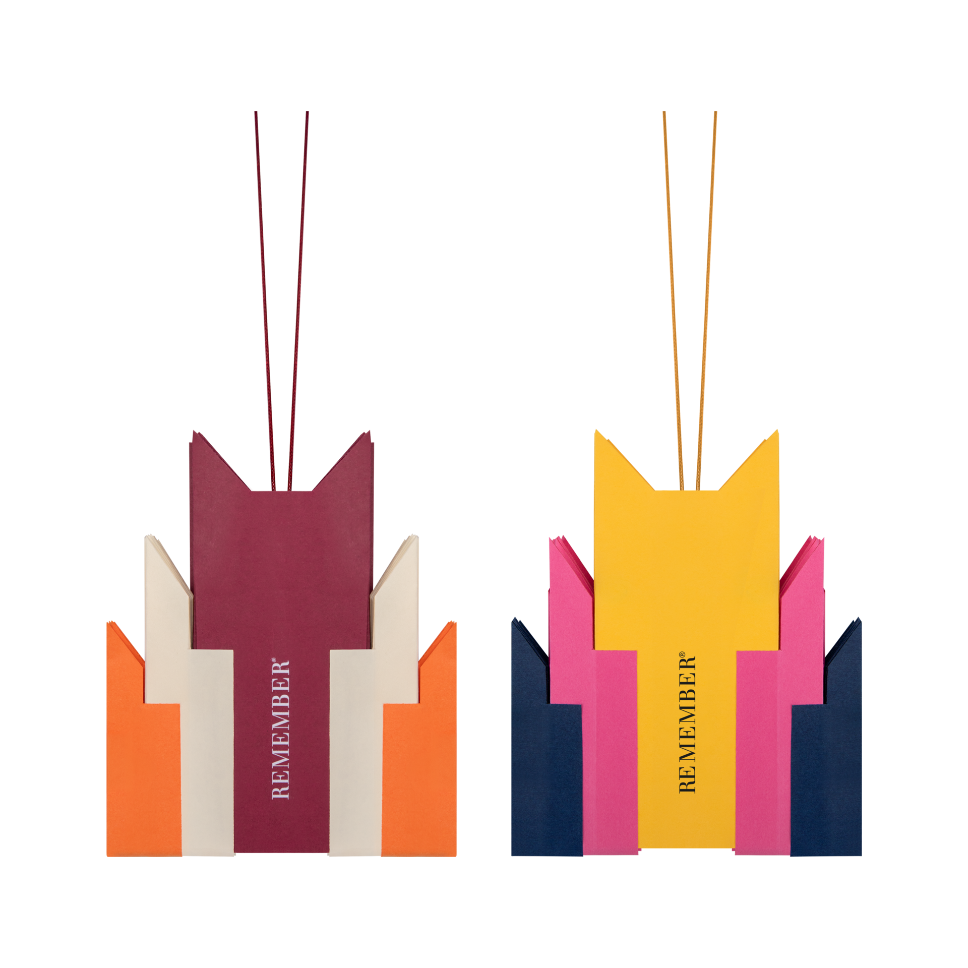Deux étoiles en papier pliées aux couleurs vives, au motif Nova, sur fond blanc. À gauche : bordeaux, beige et orange ; à droite : jaune vif, rose et bleu marine. Avec de fins cordons et l'inscription « REMEMBER ».