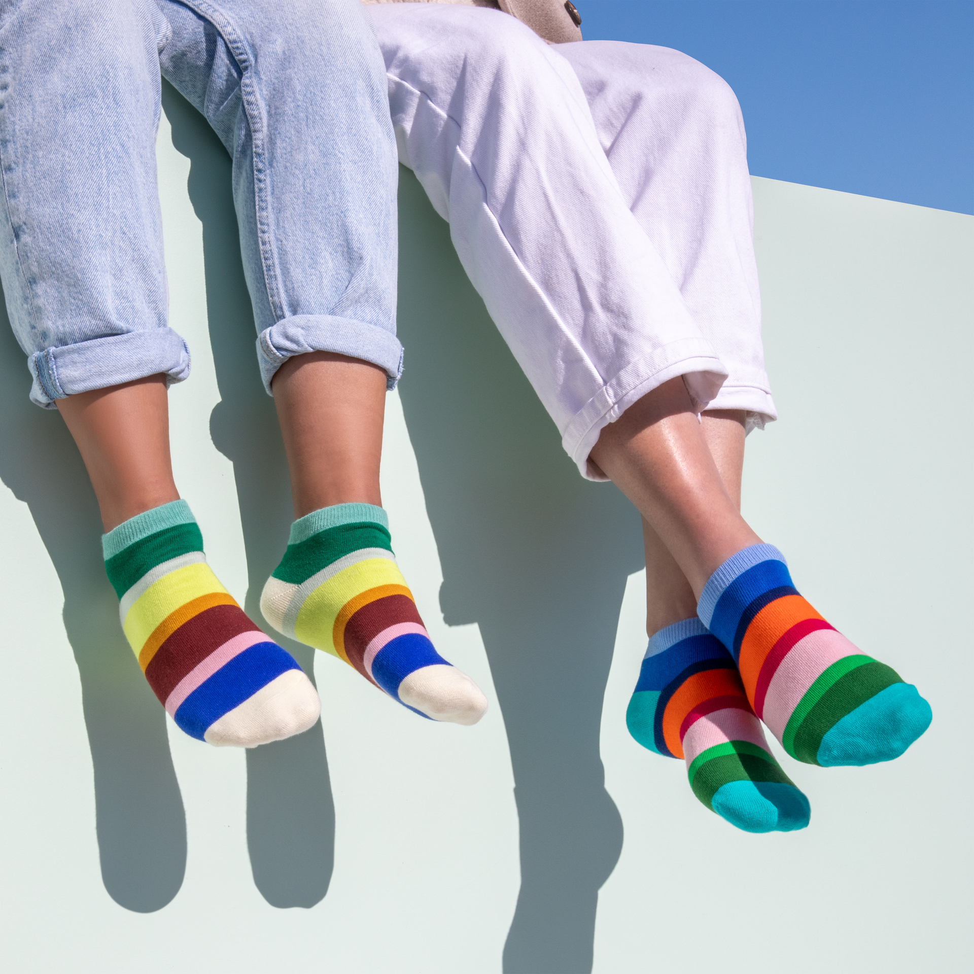 Drei Paar Sneakersocken, jedes mit bunten, horizontalen Streifen, liegen nebeneinander. Die Socken haben unterschiedliche Farbkombinationen.