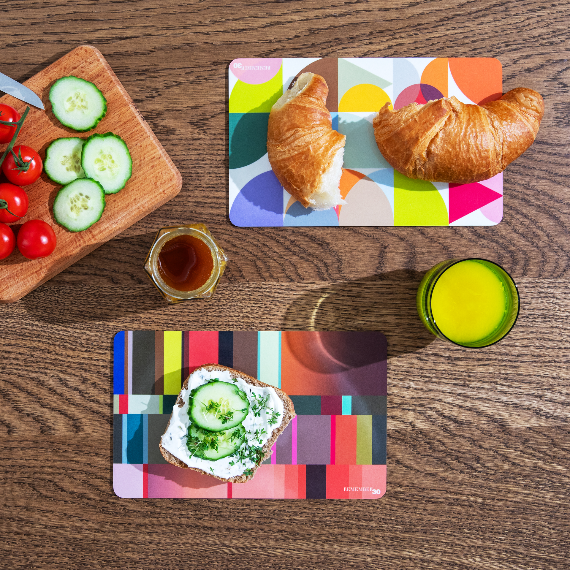 Vista dall'alto: colazione con croissant, pane con cetrioli, miele, pomodori, cetrioli su una tavola e succo d'arancia su uno sfondo colorato.