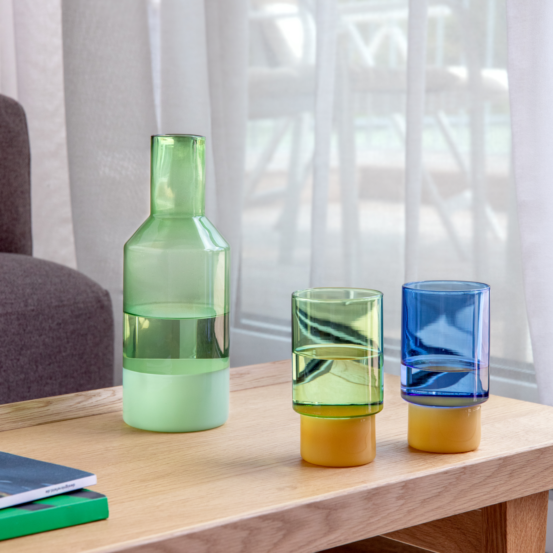 Zwei hohe zylindrische Jill Gläser (350 ml) stehen nebeneinander. Der obere Bereich ist durchscheinend blau, der untere dickere Sockel in mattem Ocker, ideal für Getränke aller Art.