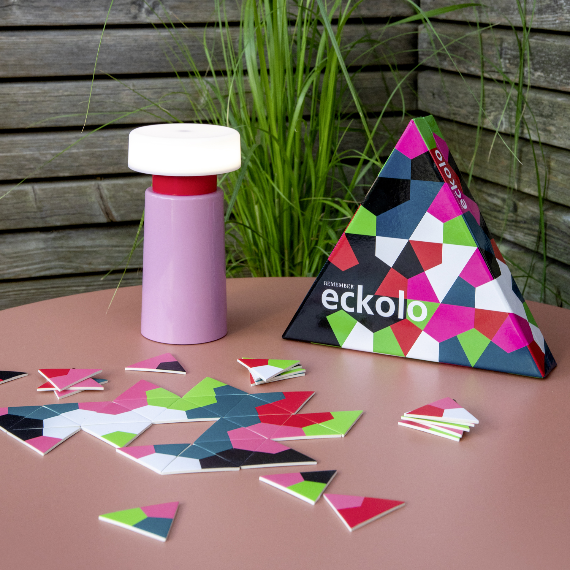 Dreieckige Spielbox von Eckolo mit farbenfrohem, geometrischem Muster in Pink, Rot, Grün, Schwarz, Weiß und Blau. Der Name des Spiels ist gut sichtbar aufgedruckt.