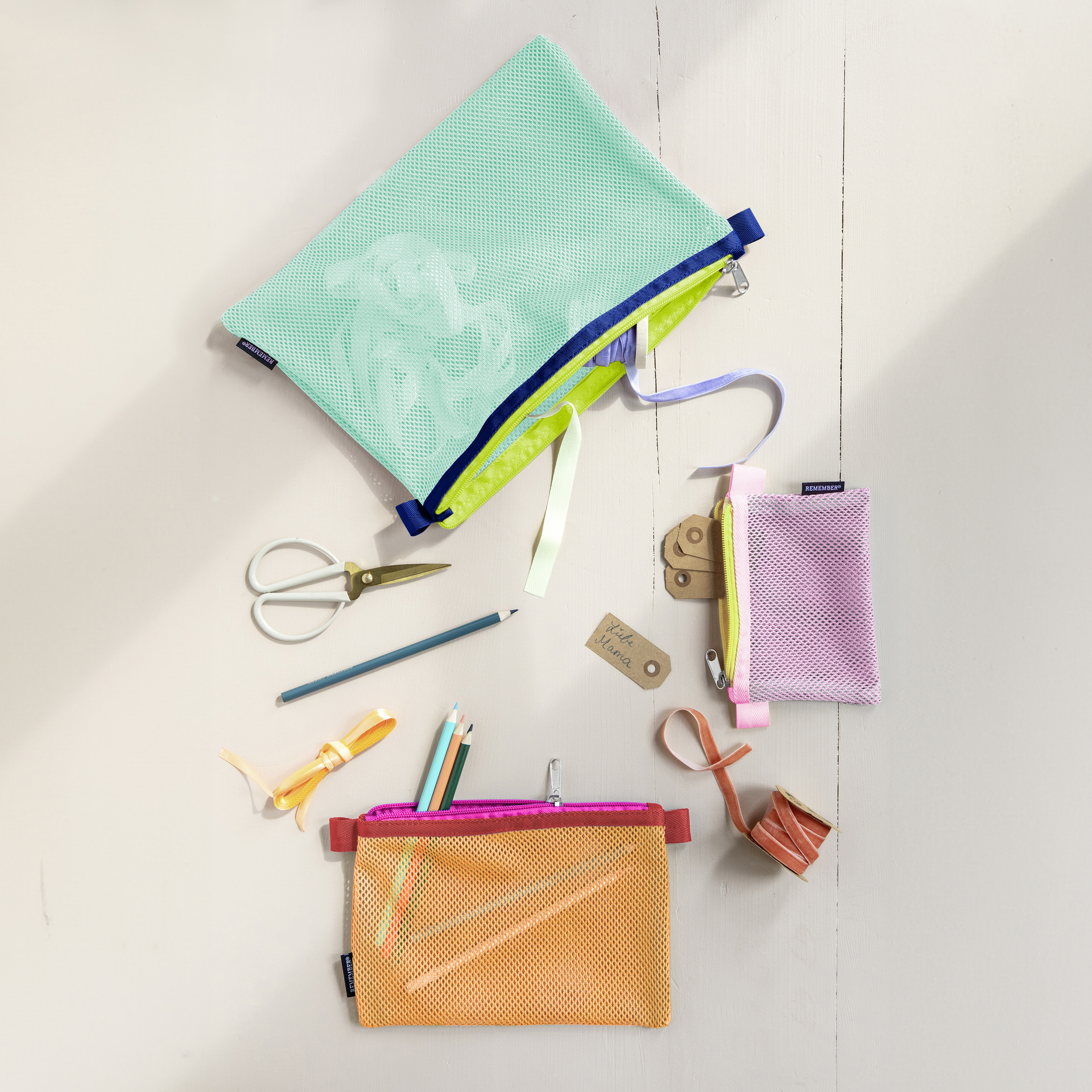 Mehrfarbige Netztaschen, Stifte, Schere, Geschenkbänder und Etikett mit Schriftzug "Liebe Mama" liegen auf hellem Untergrund.