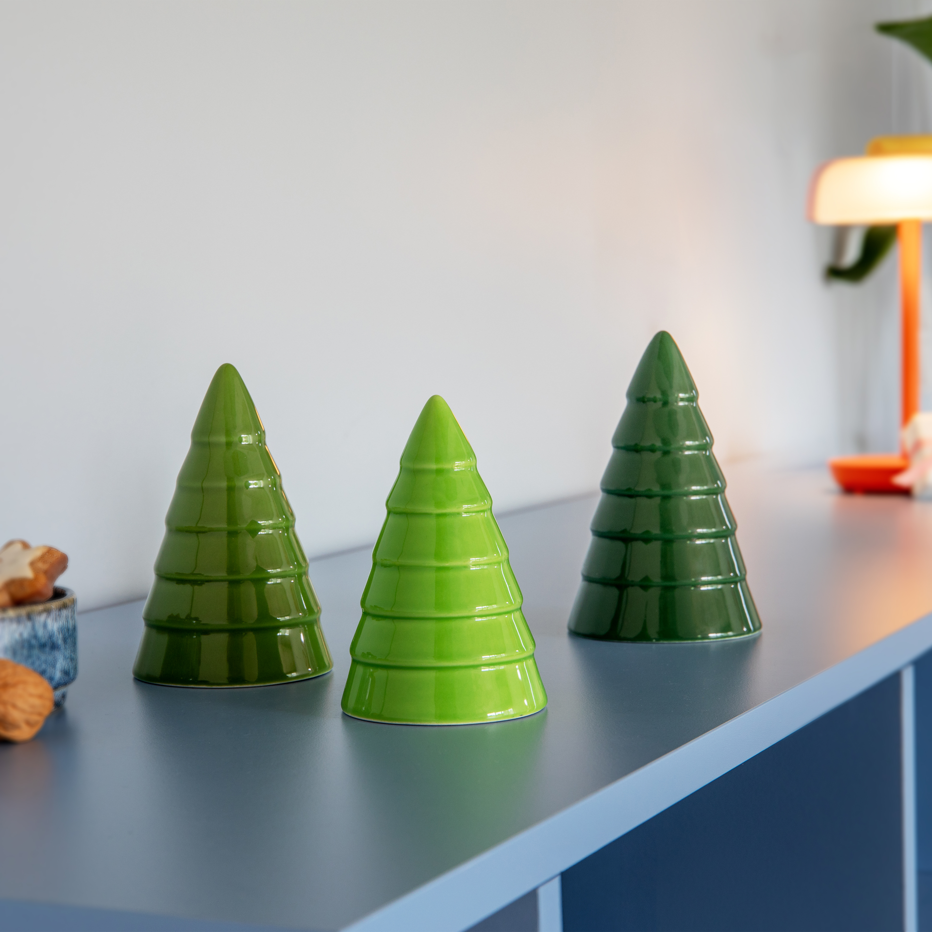 Trois sapins décoratifs en céramique sur fond blanc. De gauche à droite : vert foncé, vert moyen, vert clair. Émaillés brillants, ils présentent des rainures horizontales qui évoquent des branches stylisées et une texture en couches.