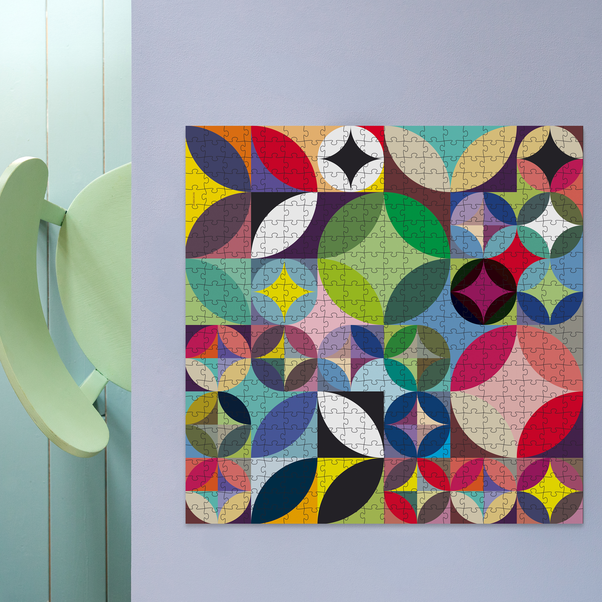 500-Teile-Puzzle „Rosetta“: buntes geometrisches Kreis- und Segmentmuster in Rot, Blau, Grün, Gelb, Violett. Daneben die schwarze zylindrische Verpackung.