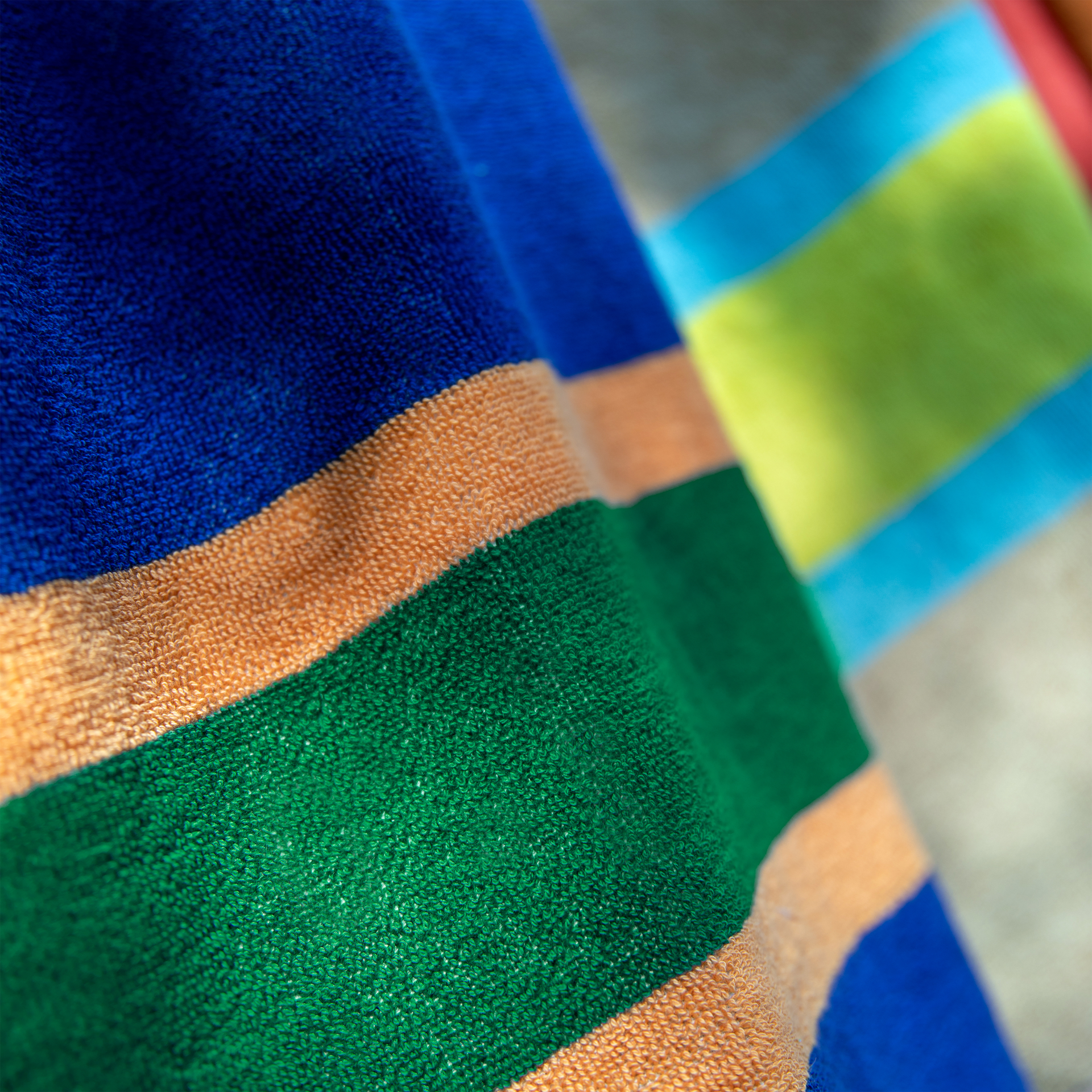 Nahaufnahme des flauschigen Badetuchs Tallinn mit breiten, farbigen Streifen in Dunkelblau, leuchtendem Orange und kräftigem Grün. Die Frottee-Baumwolltextur betont Saugfähigkeit und Weichheit des extragroßen Handtuchs.