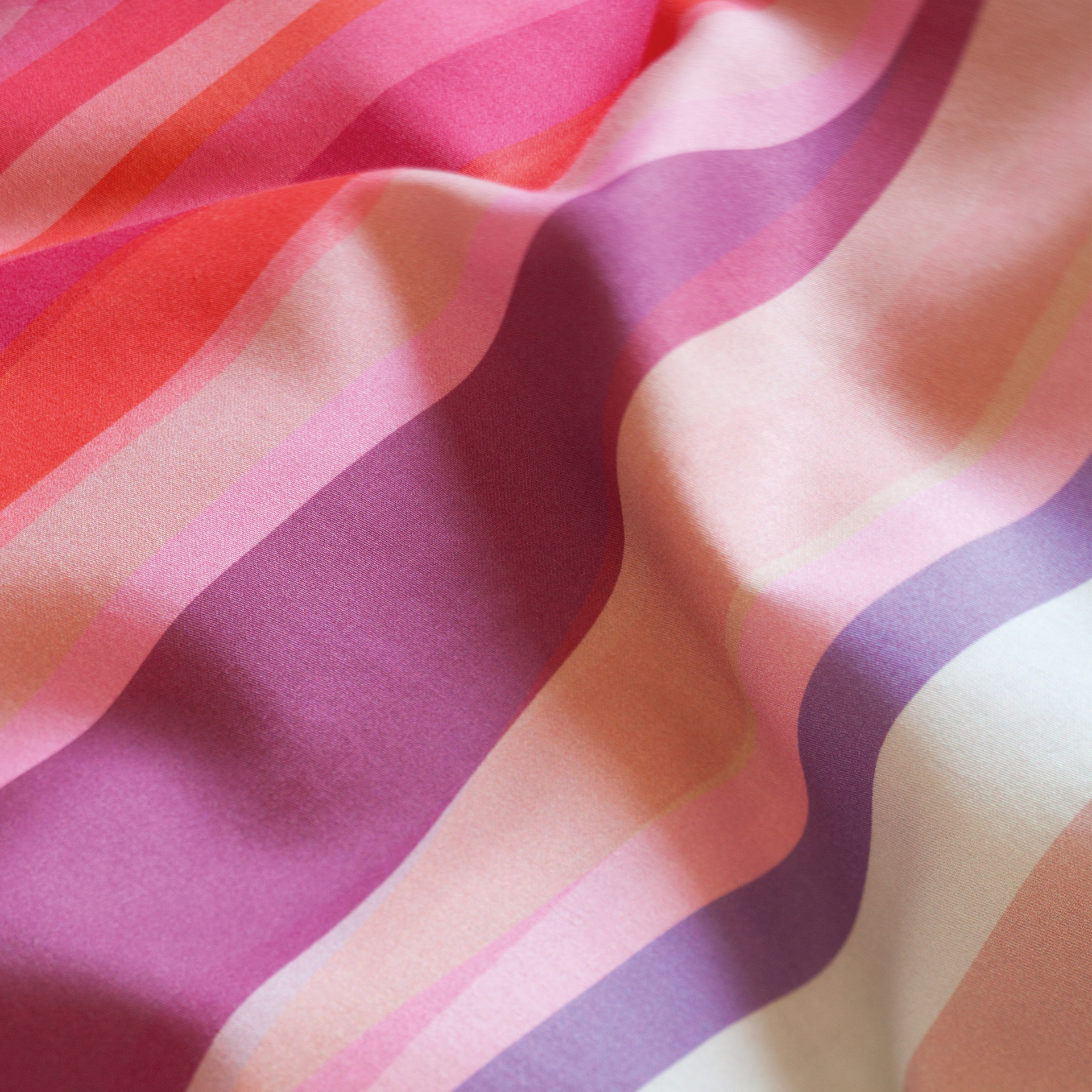Detailaufnahme der 'Mateo' Bettwäsche mit gewellten, horizontalen Streifen in Pink-, Rot- und Lilatönen. Der Stoff wirkt weich und hochwertig.