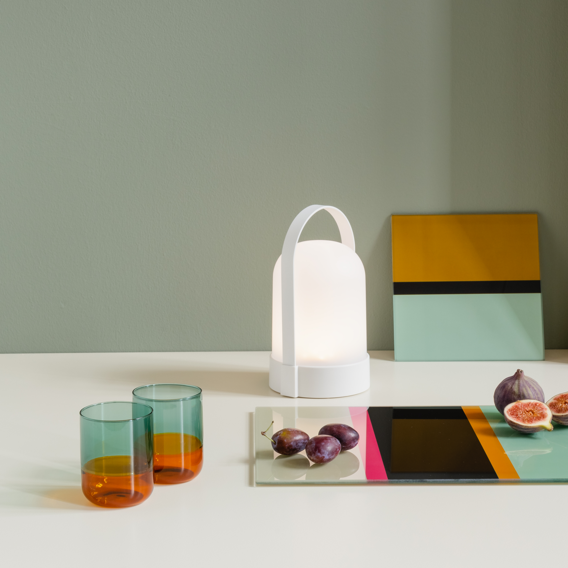 Zwei 'amber' Gläser, eine Lampe und Früchte auf einem Tisch. Die Gläser sind zweifarbig, oben blau und unten bernsteinfarben.