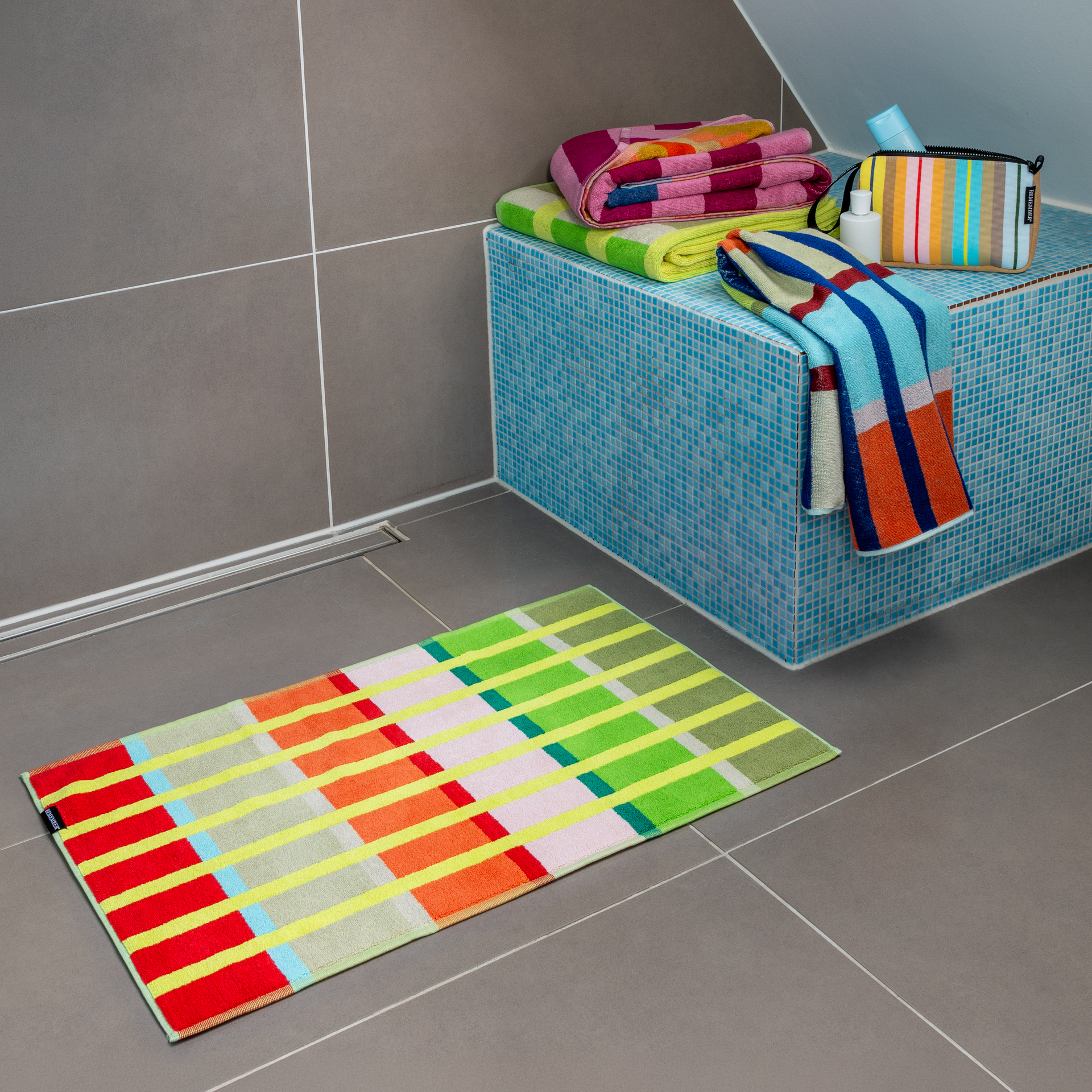 Un tapis de salle de bain Kaido rectangulaire au motif rayé très vivant. De larges rayures horizontales jaunes viennent rompre l'uniformité des blocs de couleur verticaux dans les tons marron, vert, rose clair, corail, rouge, bleu clair et gris.