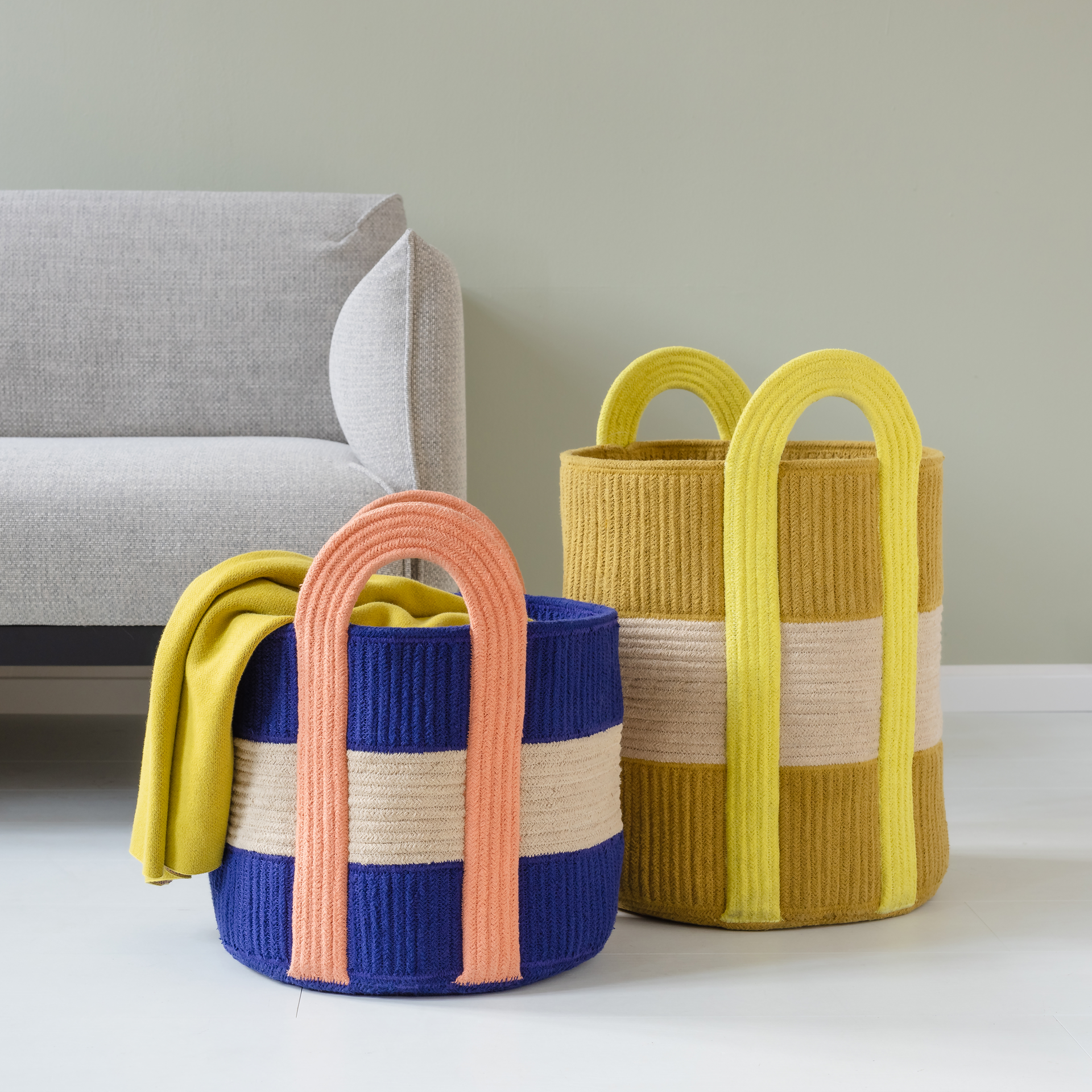 Ein kleiner, zylinderförmiger Korb in Blau und Beige mit orangefarbenen Tragegriffen.