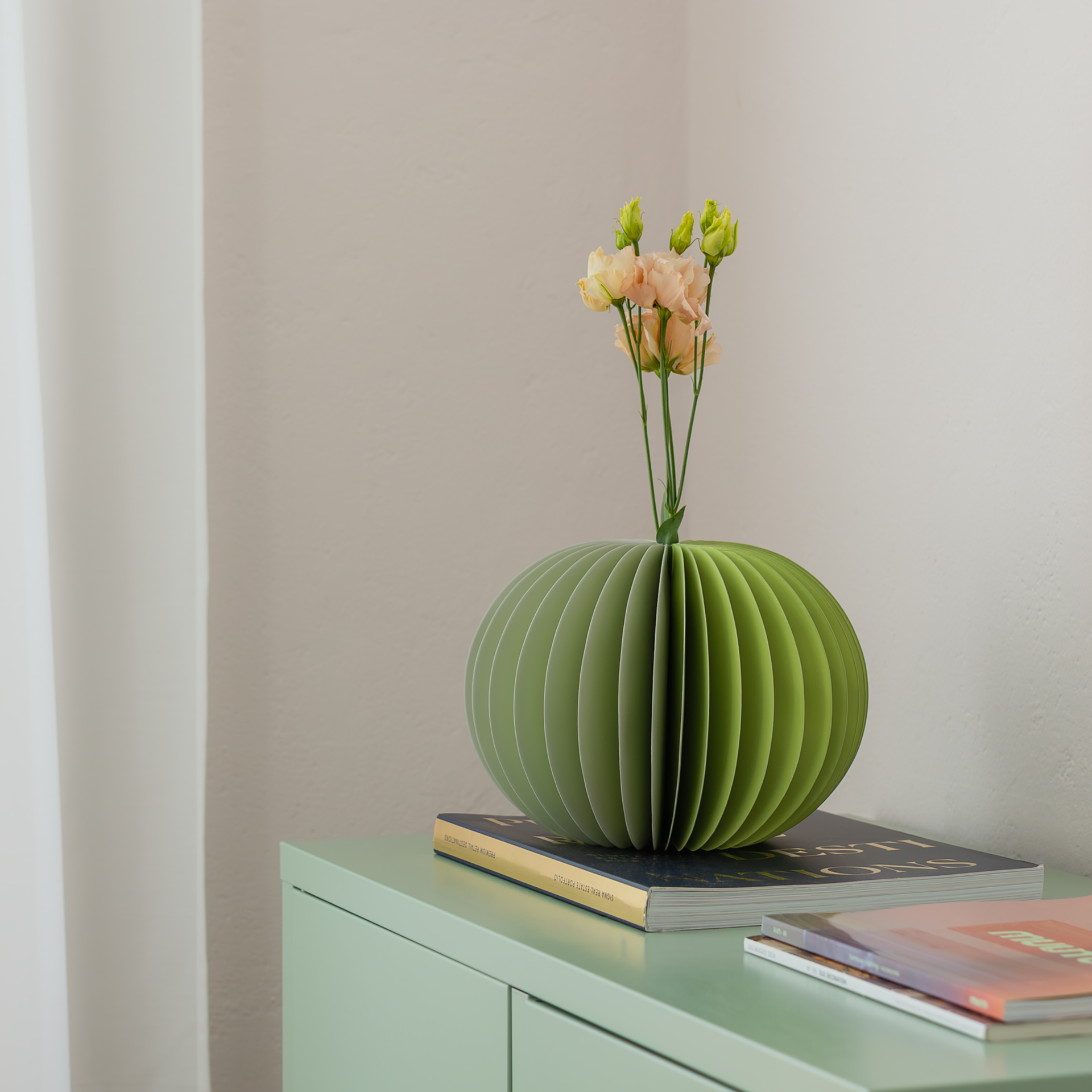 Eine runde, zweifarbige Papiervase 'Yuki' in Salbei- und Grautönen. Die Vase besteht aus gefalteten Papiersegmenten.
