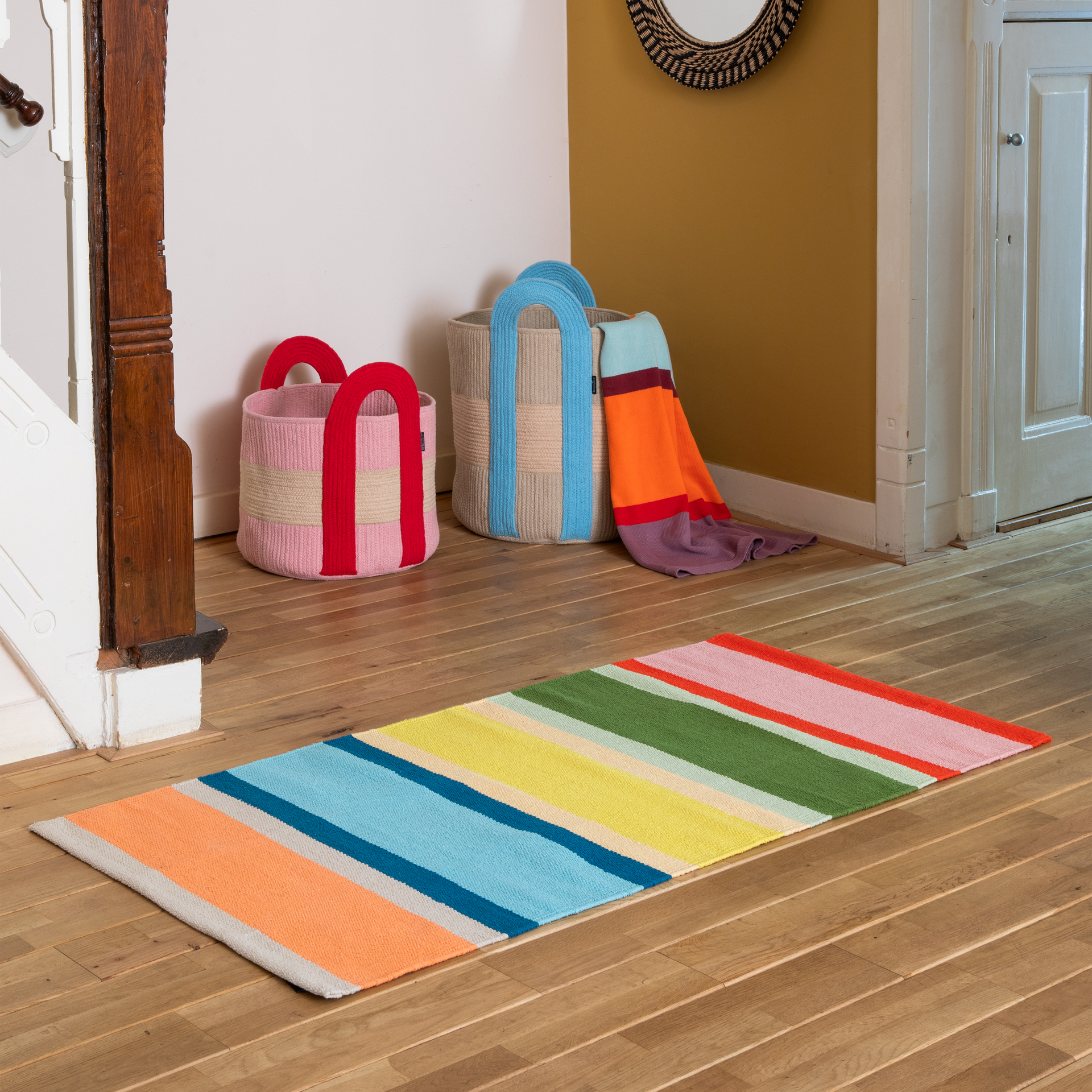 Tapis de passage coloré à rayures verticales dans des tons de rouge vif, rose tendre, vert olive, jaune vif, turquoise, bleu clair et orange corail, séparées par d'étroites bandes de couleur crème. Poils courts pour une touche de gaieté.