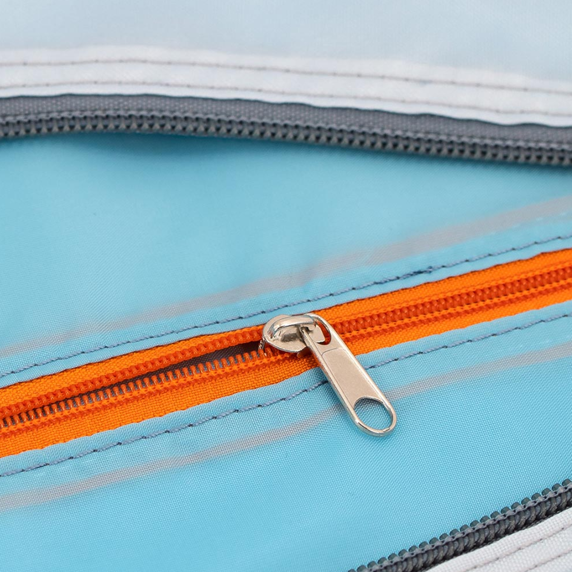 Detailaufnahme einer geöffneten Freizeit- & Reisetasche 'Tom' mit orangefarbenem Reißverschluss und hellblauem Innenfutter. Der Reißverschluss-Zipper ist aus Metall.