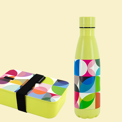 Ein gelber Lunch-Container mit schwarzem Band und eine Trinkflasche mit geometrischem Design sind auf einem beigen Untergrund platziert.