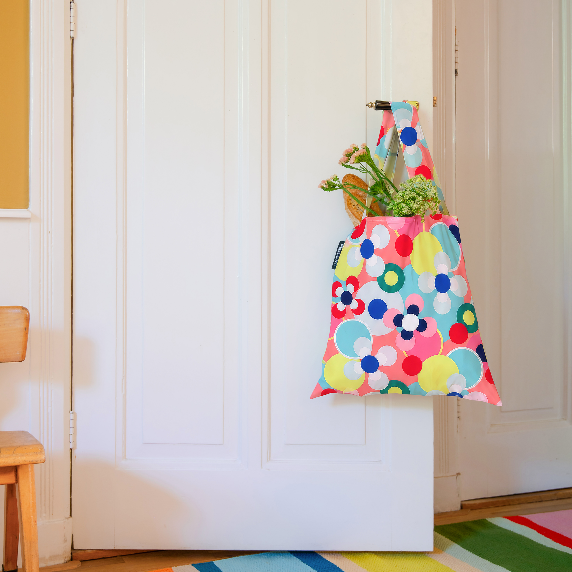 Sac de transport coloré et pliable, orné d’un motif abstrait accrocheur composé de cercles et de fleurs stylisées dans des tons de rose, rouge, bleu, jaune et turquoise sur un fond rouge corail. Doté de deux poignées et d’une étiquette «REMEMBER 30 ».