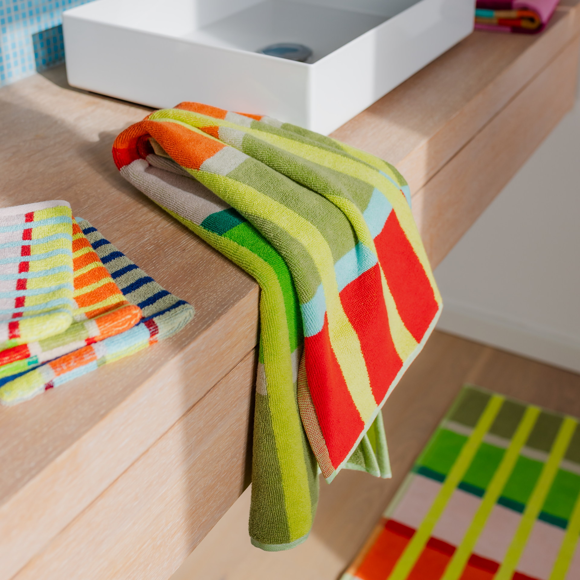 Serviette Kaido pliée, ornée d'un motif à carreaux éclatant : rayures verticales jaunes et bandes horizontales vives. Le gris-brun, blanc, vert, rose, corail, bleu clair et rouge lui donnent un look joyeux.