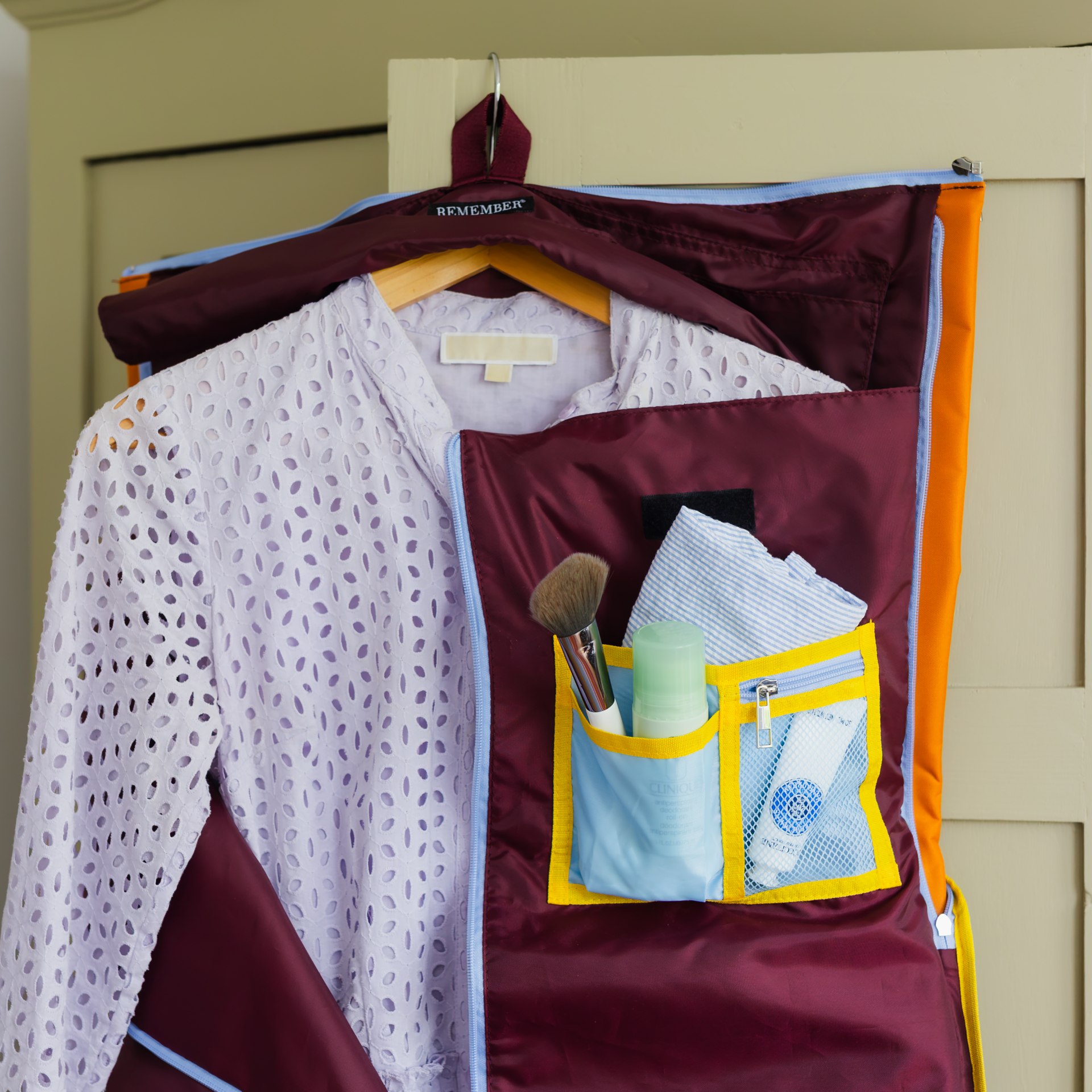 Sac de voyage Lennard bordeaux foncé, ouvert et suspendu à un crochet. Un vêtement violet clair à mailles ajourées, sans plis, est sur un cintre en bois dans le compartiment principal. À droite, poches avec brosse, déodorant et tube cosmétique.