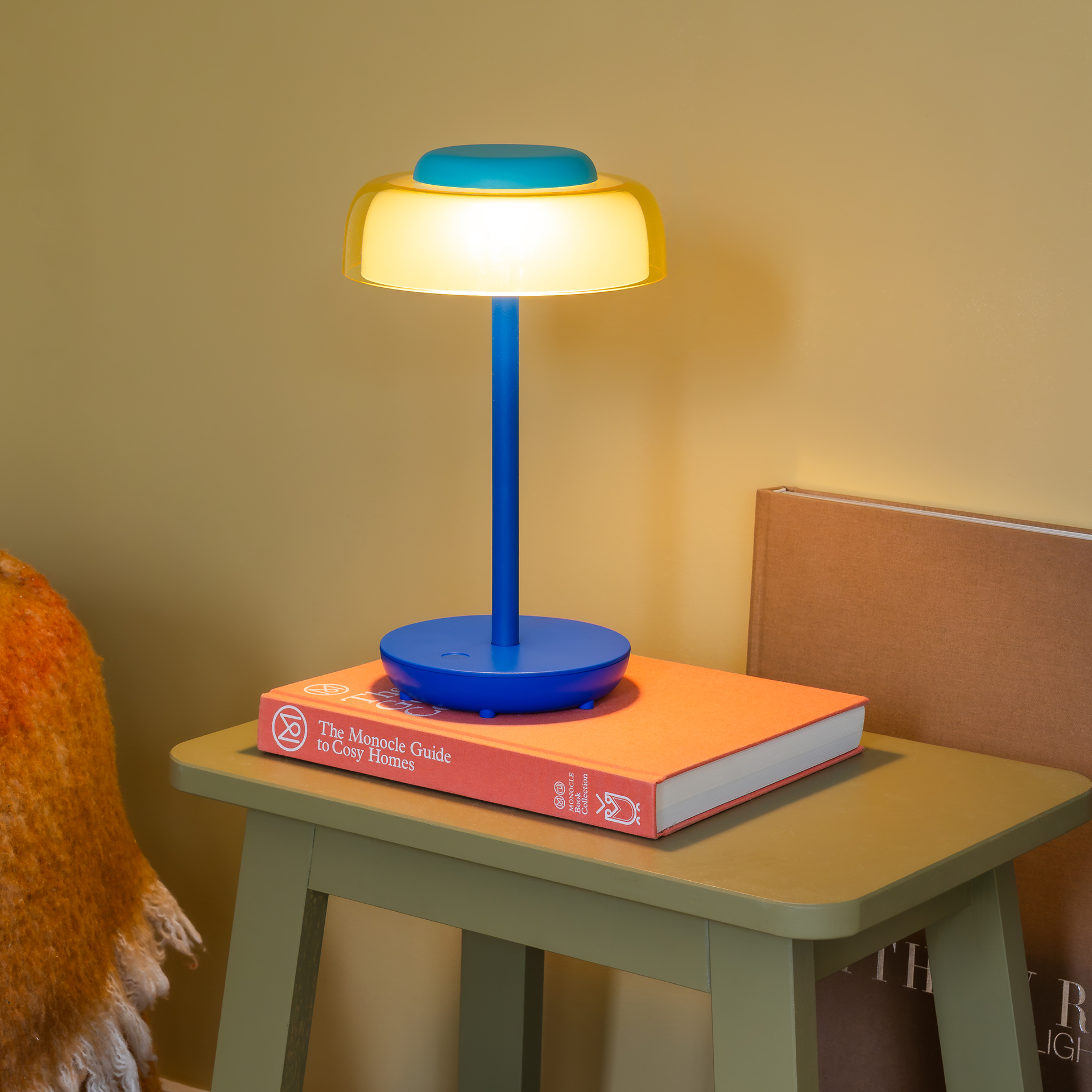 Moderna lampada da tavolo senza fili Juno con elegante base blu scuro e base rotonda. Paralume giallo trasparente con cupola trasparente. La superficie touch piatta color turchese e il simbolo di accensione/spegnimento indicano un funzionamento intuitivo.