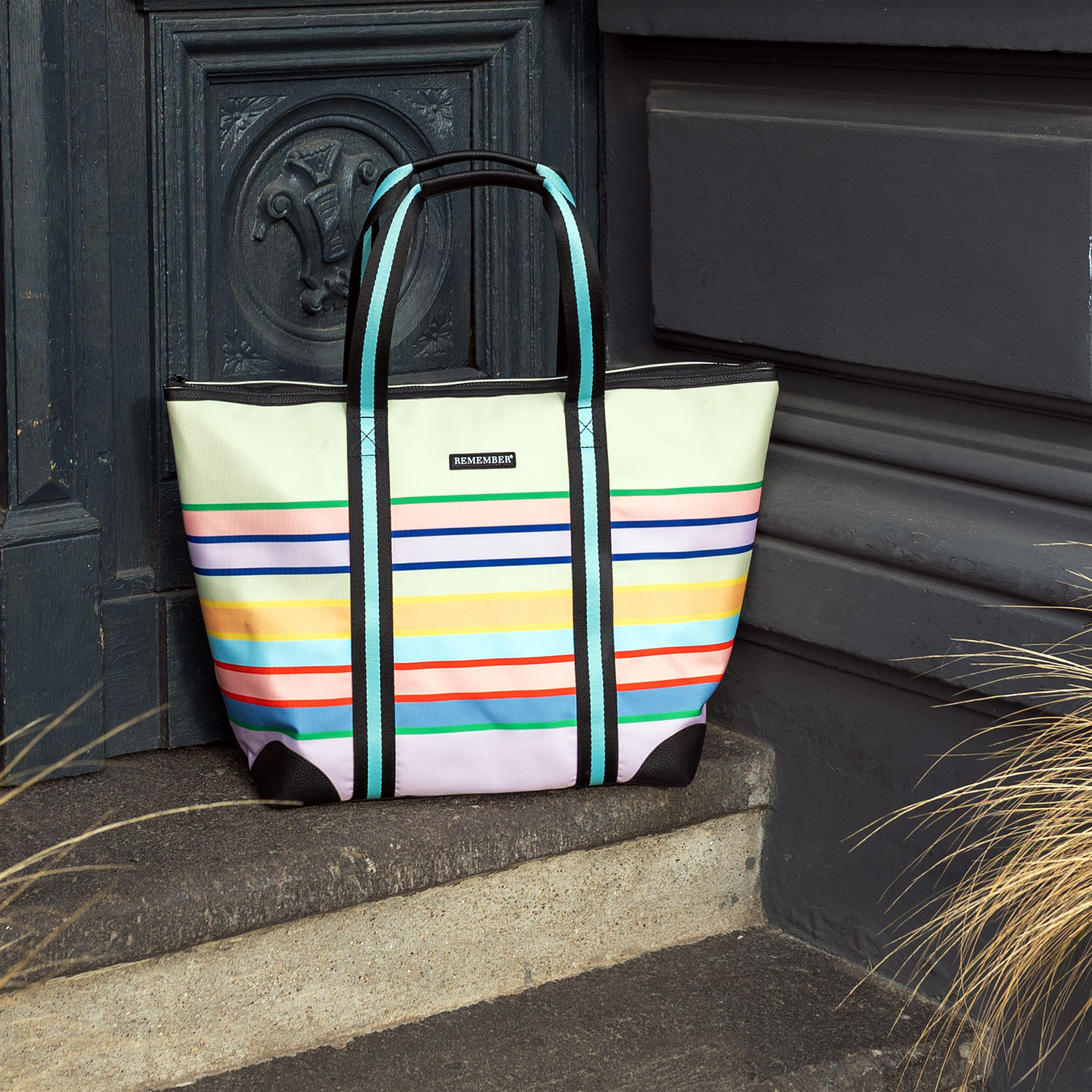 Gestreifte Levante Shopper Tasche mit gelbem Oberteil, farbigen horizontalen Streifen und schwarzen Trägern mit hellblauen Akzenten.