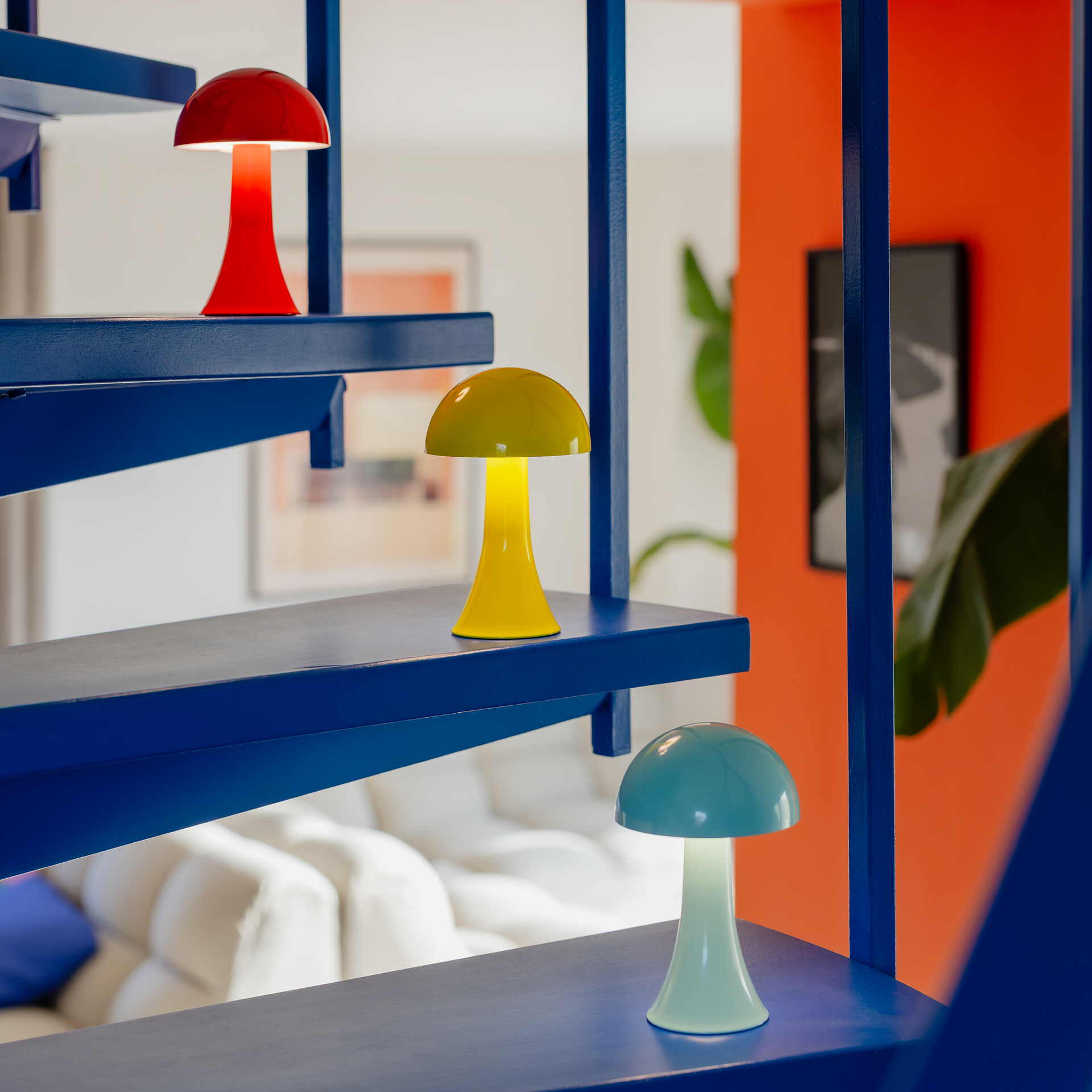 Auf einer blauen Treppe stehen drei pilzförmige Lampen in Rot, Gelb und Türkis. Sie leuchten hell und setzen Farbakzente in der modern eingerichteten Wohnung.