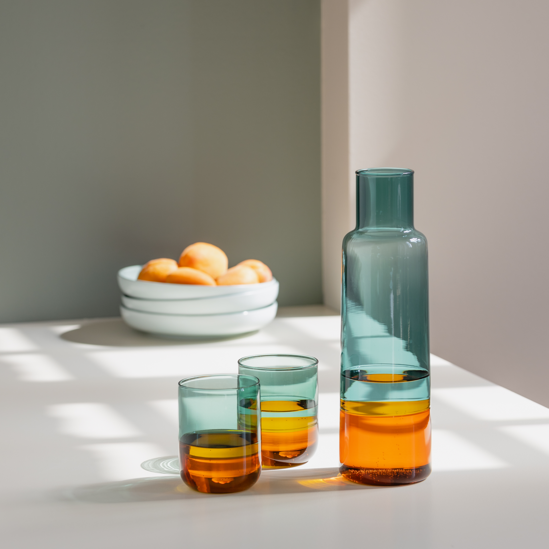 Schlanke, hohe Glaskaraffe. Der obere Teil ist grün, der untere Teil bernsteinfarben. Die Übergänge sind fließend. Transparenter, leerer Behälter aus Glas.
