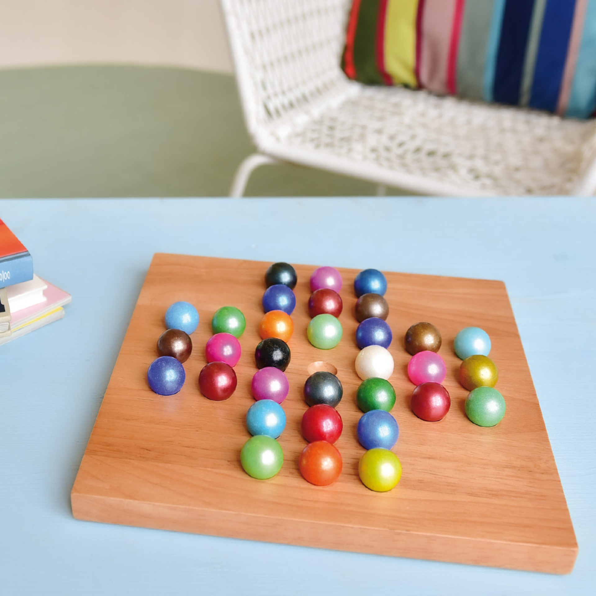 Planche en bois avec des boules de verre colorées dans un motif de jeu solitaire. En arrière-plan, une chaise et un coussin.