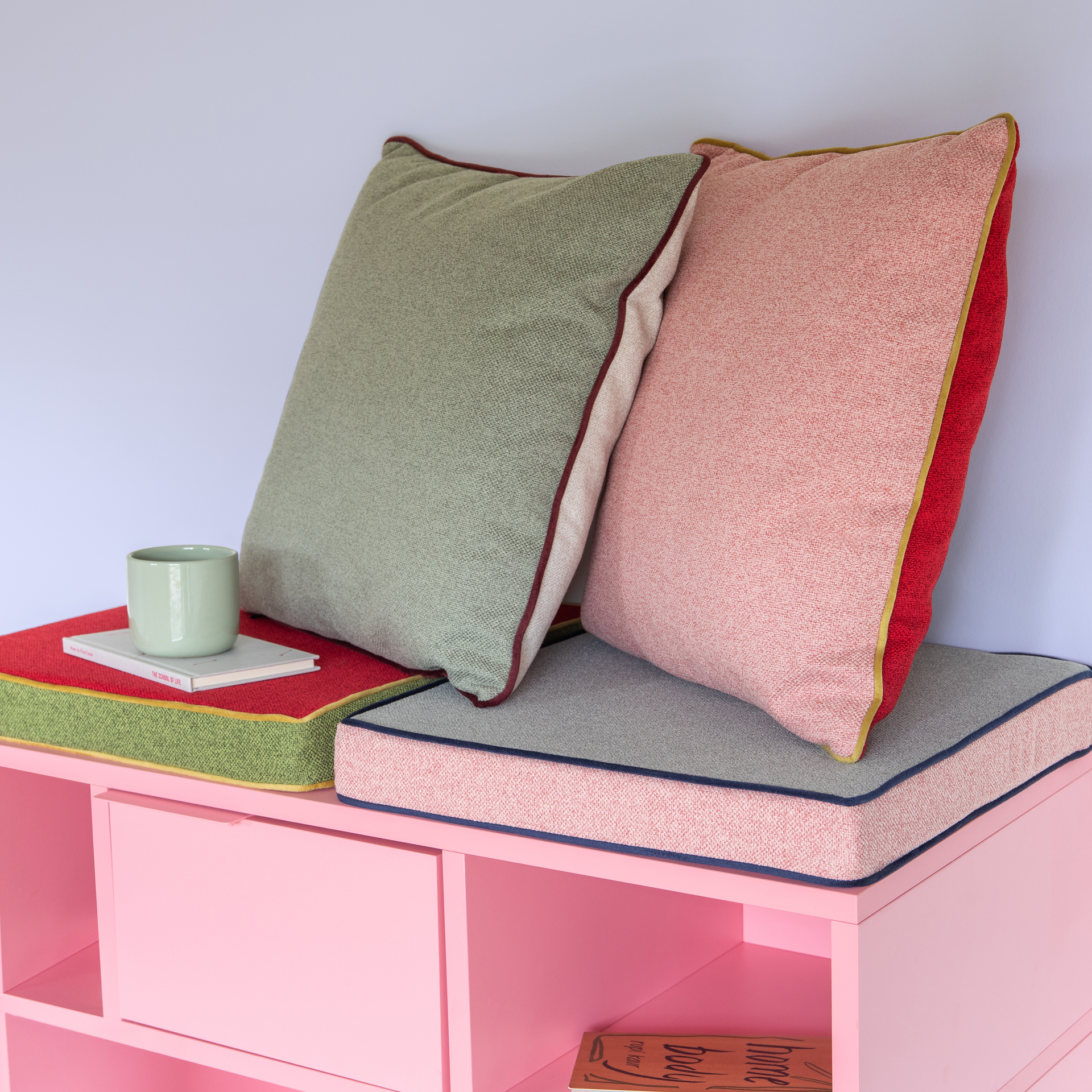 Zwei Kissen in Rosa und Cranberry-Rot mit grüner Paspel liegen übereinander. Das vordere Kissen ist rosa und leicht nach links geneigt.