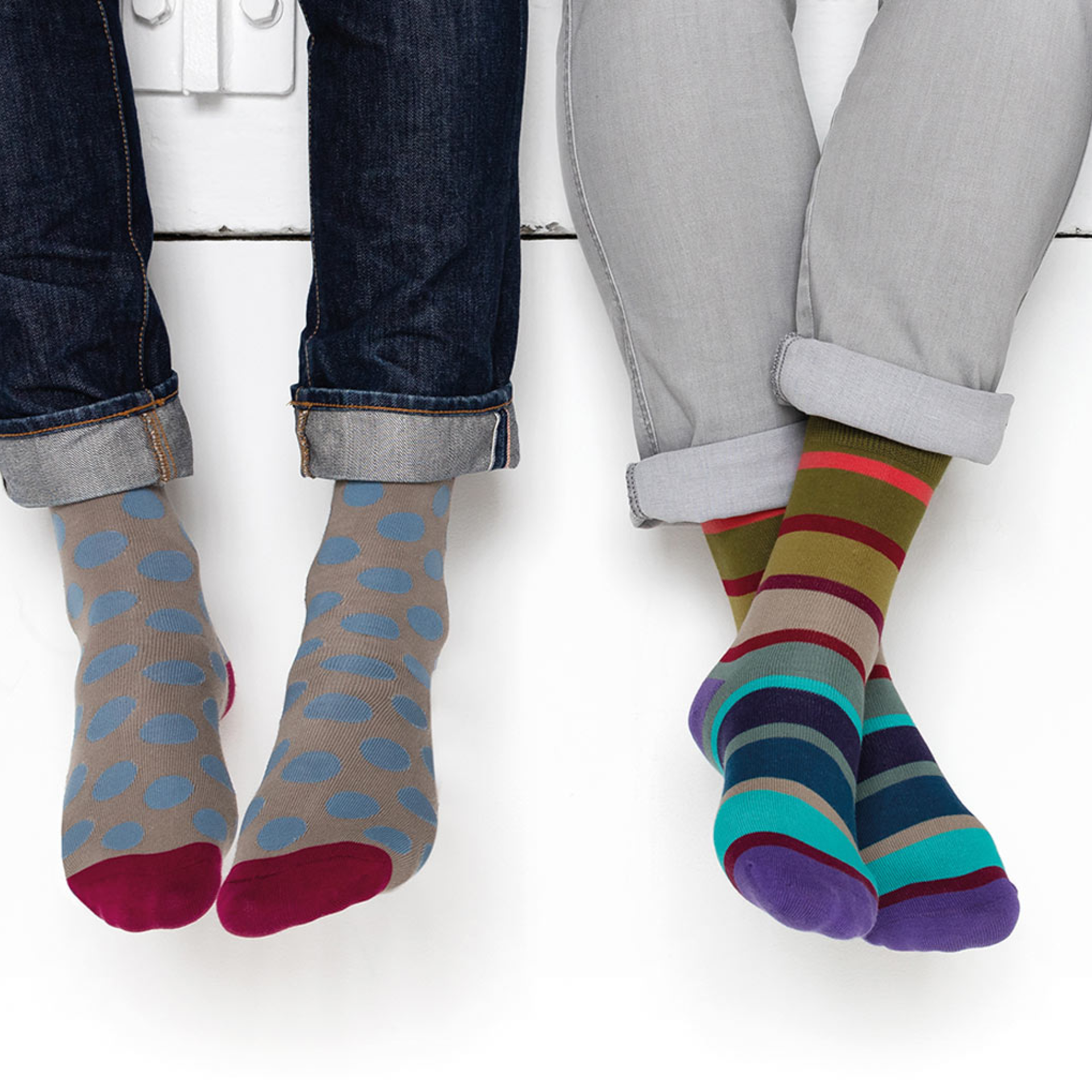 Zwei Personen tragen bunte Socken der Größe 41-46. Links Socken mit blauen Punkten, rechts gestreifte Socken in lila, grün und blau.