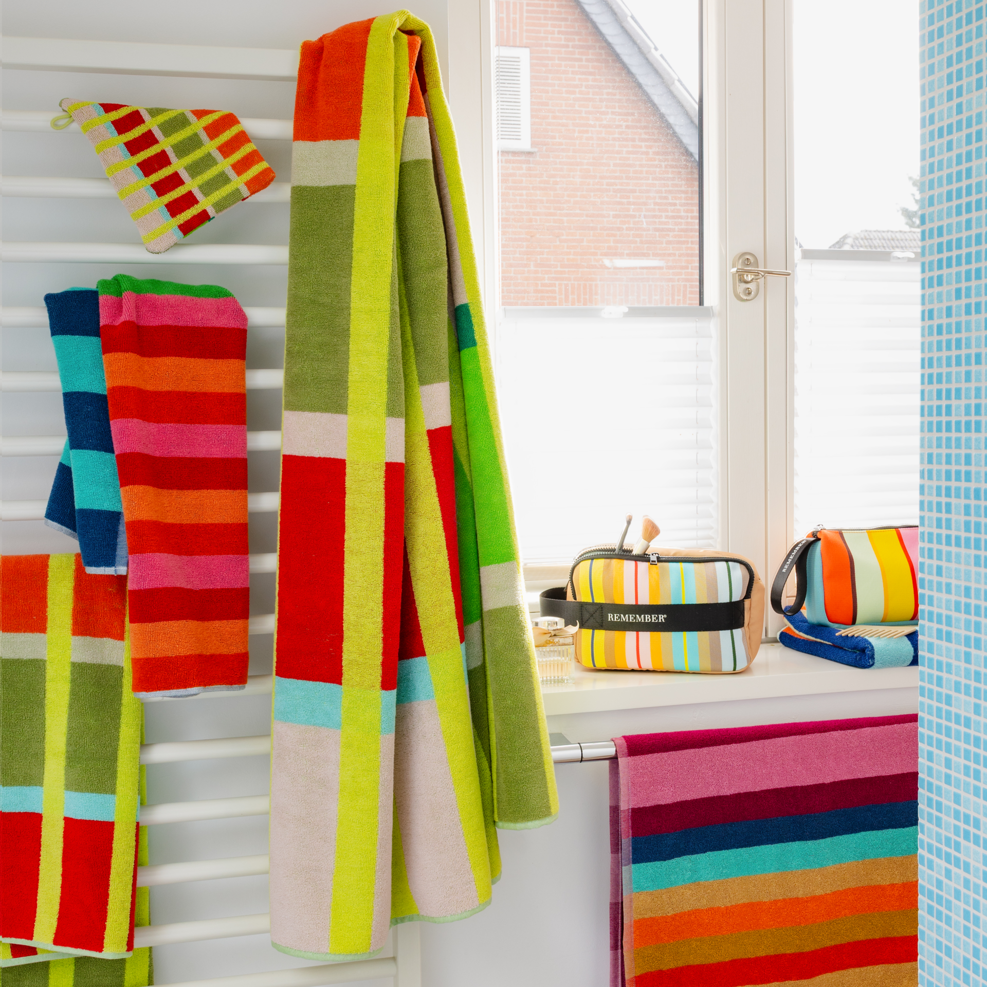 Serviette de bain Kaido à motif vertical coloré en damier : grands blocs horizontaux rose pastel, rouge, vert clair et gris-brun, avec fines rayures verticales jaune clair et étroites rayures blanches et bleu clair.