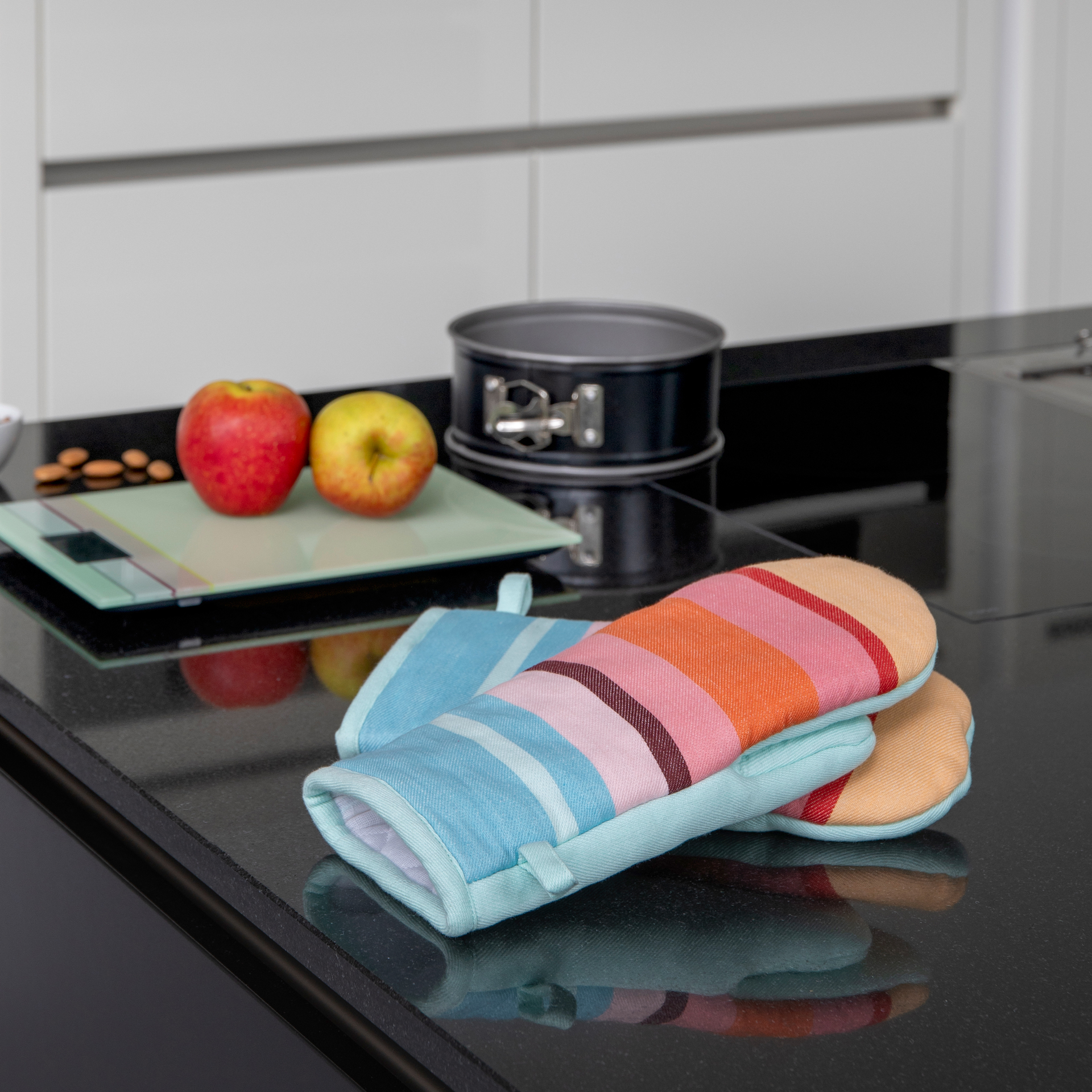 Zwei Ofenhandschuhe im Set, gestreift in Gelb, Rosa, Orange und Blau. Die Handschuhe sind hellgrün umrandet und haben eine Schlaufe zum Aufhängen.