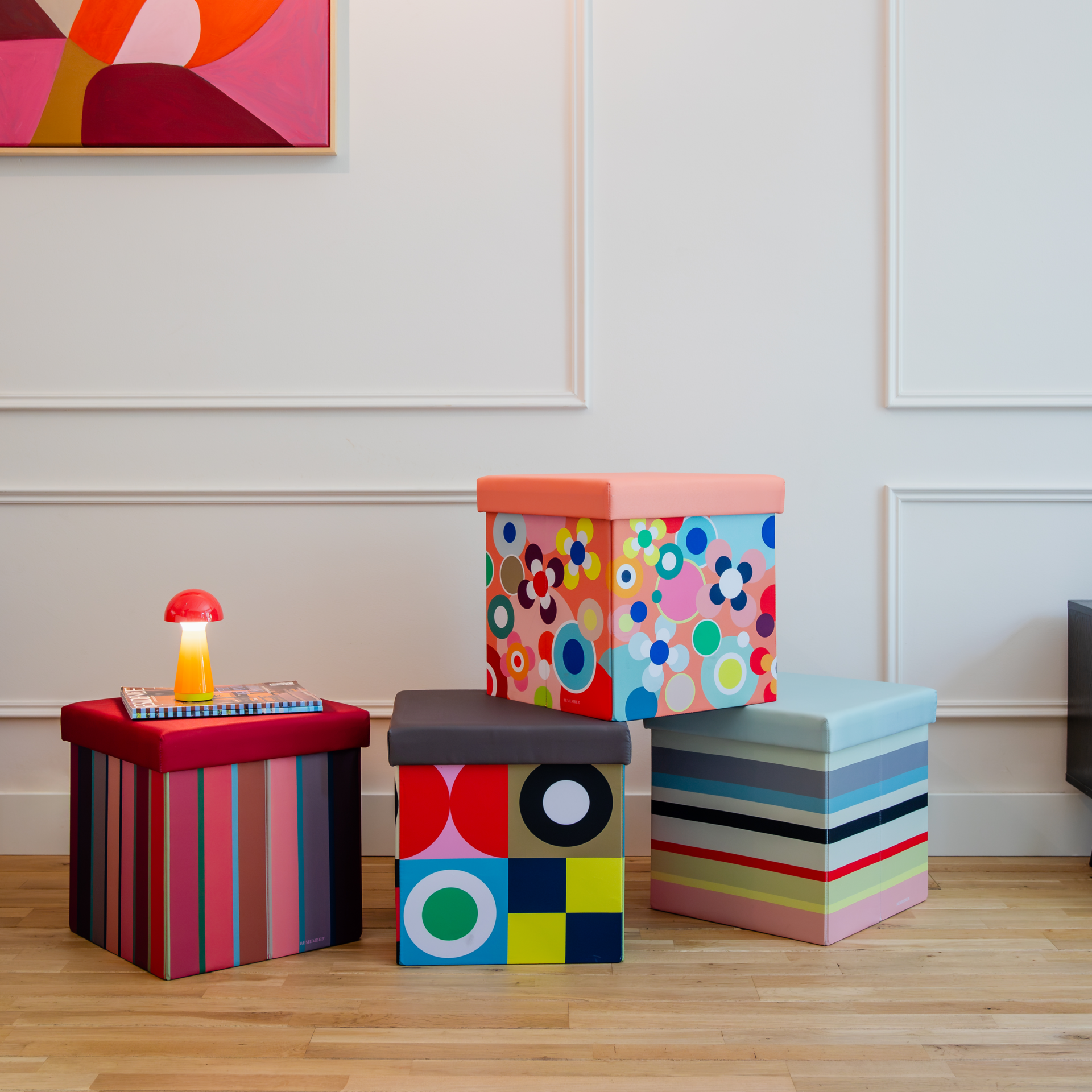 Banc carré avec rangement, recouvert d'un coussin vert olive foncé. Côtés ornés d'un motif géométrique vif : carrés colorés, cercles, rayures et formes abstraites en tons turquoise, vert citron, orange et jaune.
