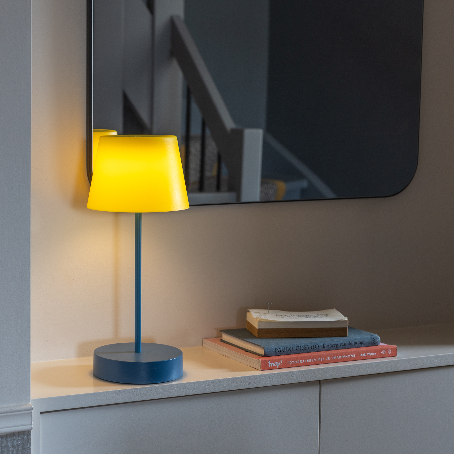 Freigestellte LED-Tischleuchte 'Oscar' in 'midnight'. Blauer, zylinderförmiger Fuß, schlanker Stab. Der Lampenschirm ist gelb, erzeugt ein warmes Licht. Minimalistisches Design.