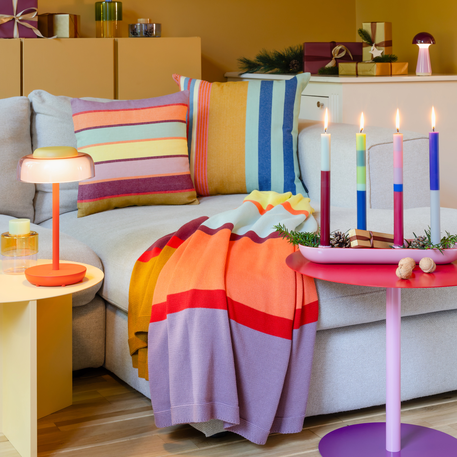 Morbida coperta lavorata a maglia Livo con un vivace motivo a righe. La coperta in cotone presenta larghe righe orizzontali nei colori giallo senape, rosso bordeaux, corallo, rosa chiaro, giallo, verde menta, arancione e blu tortora, con linee rosse.