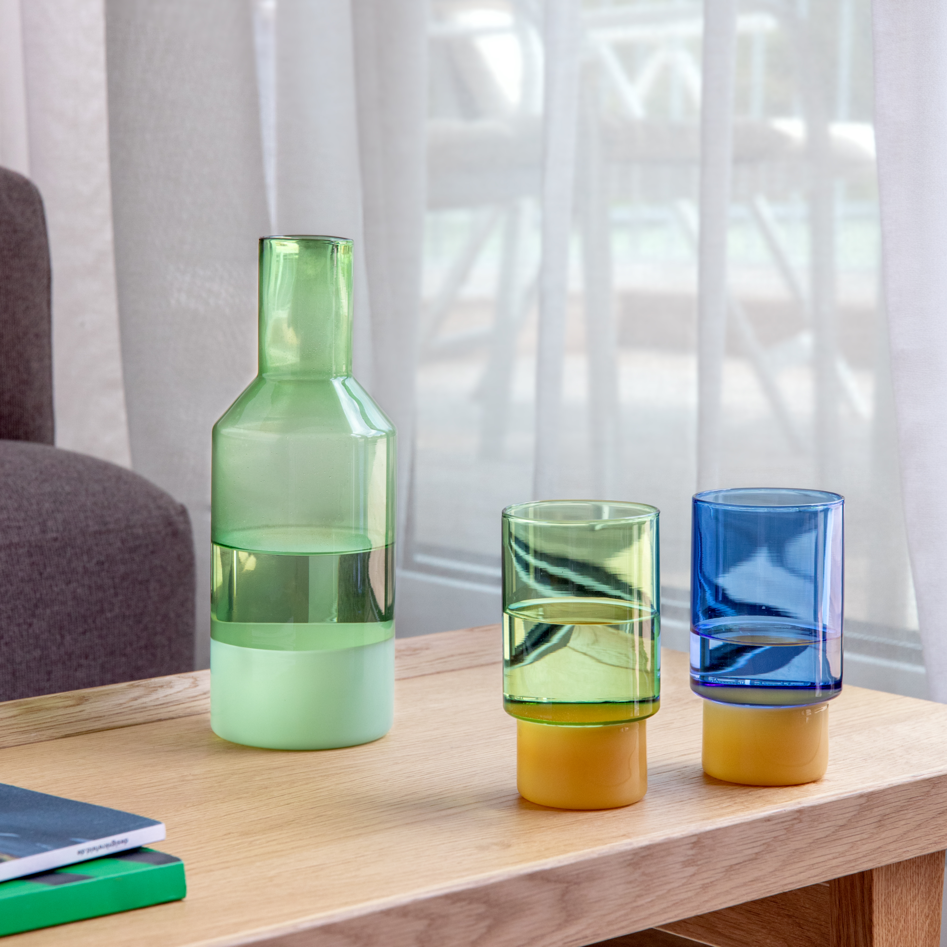 Zwei hohe, zylindrische Trinkgläser aus Borosilikatglas stehen nebeneinander. Jedes Glas hat oben einen transparenten hellgrünen Bereich und unten einen kürzeren, matten orangefarbenen Sockel. Auf weißem Hintergrund.