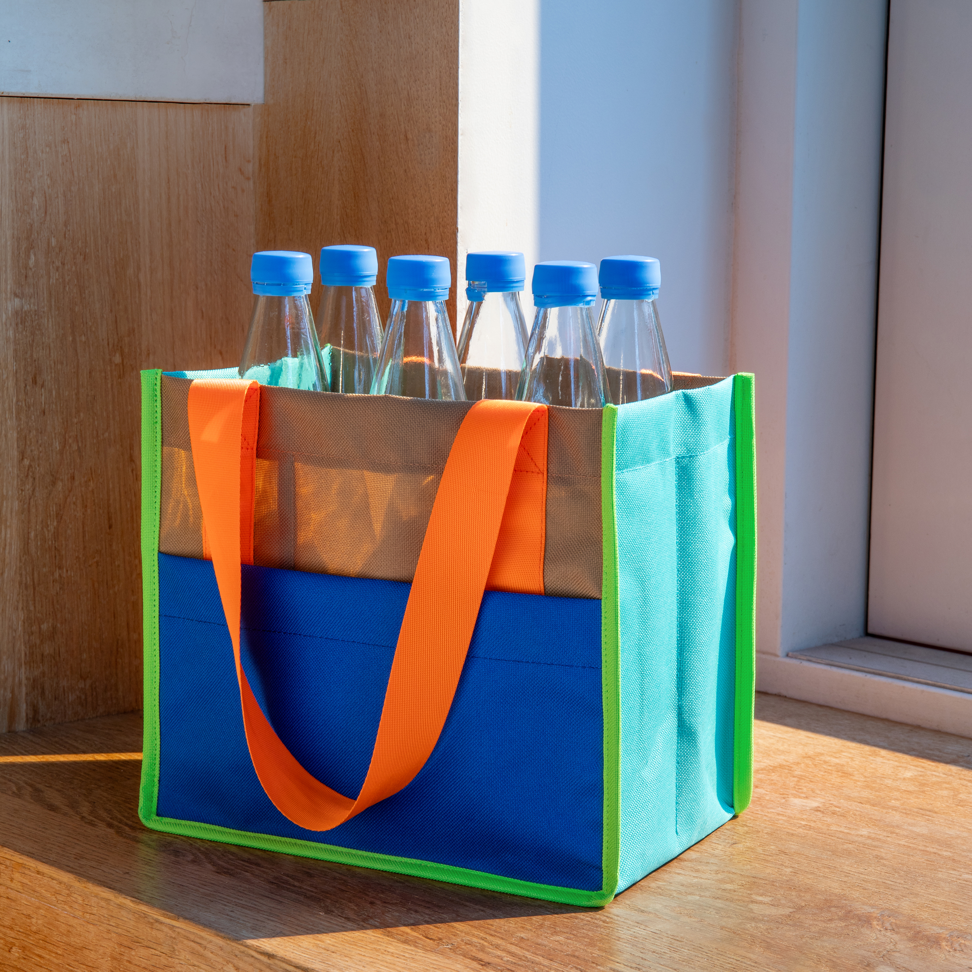 Flaschentasche 'Ocean' mit sechs Wasserflaschen, blaue Deckel, orange Trageriemen, farbenfrohes Design in blau, grün und braun.
