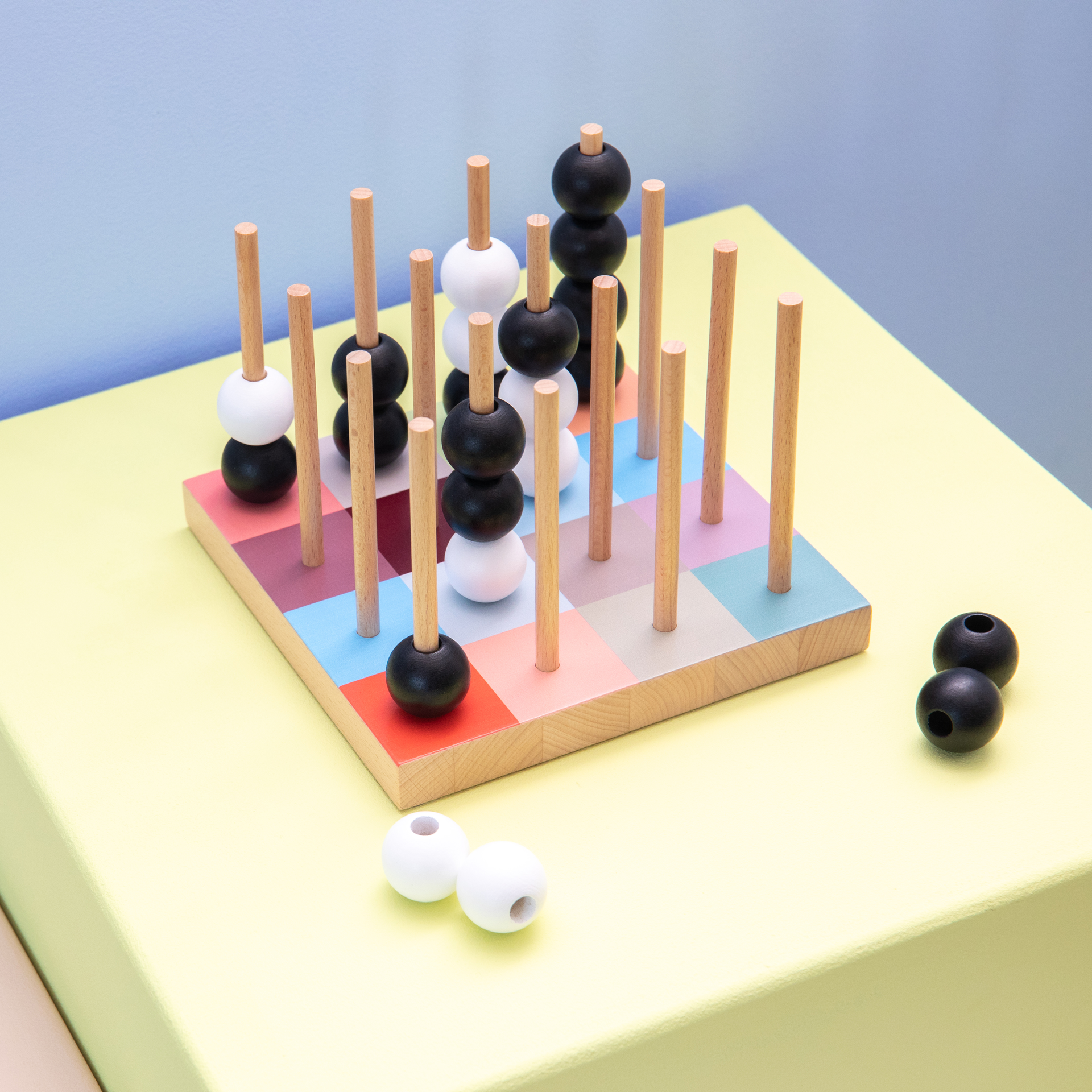 Ein SOGO-Spiel mit Holzstäben und bunten Feldern. Schwarze und weiße Kugeln sind auf die Stäbe gesteckt. Einige Kugeln liegen daneben.