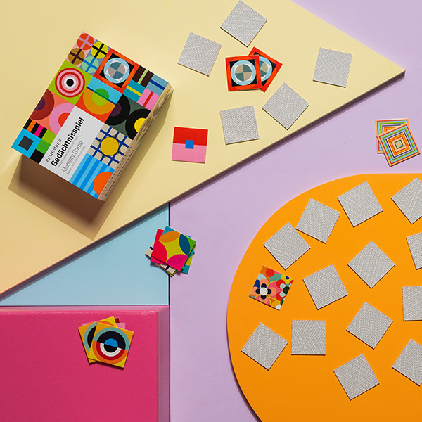 Farbenfrohes Memory-Spiel mit abstrakten Mustern, teilweise aufgedeckt, auf geometrischen Flächen in Gelb, Orange, Lila, Blau und Pink.