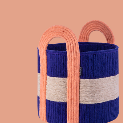 Gestrickter Korb in Blau, Beige und Apricot. Der Korb ist zylindrisch mit horizontalen Streifen und verfügt über zwei apricotfarbene Henkel.